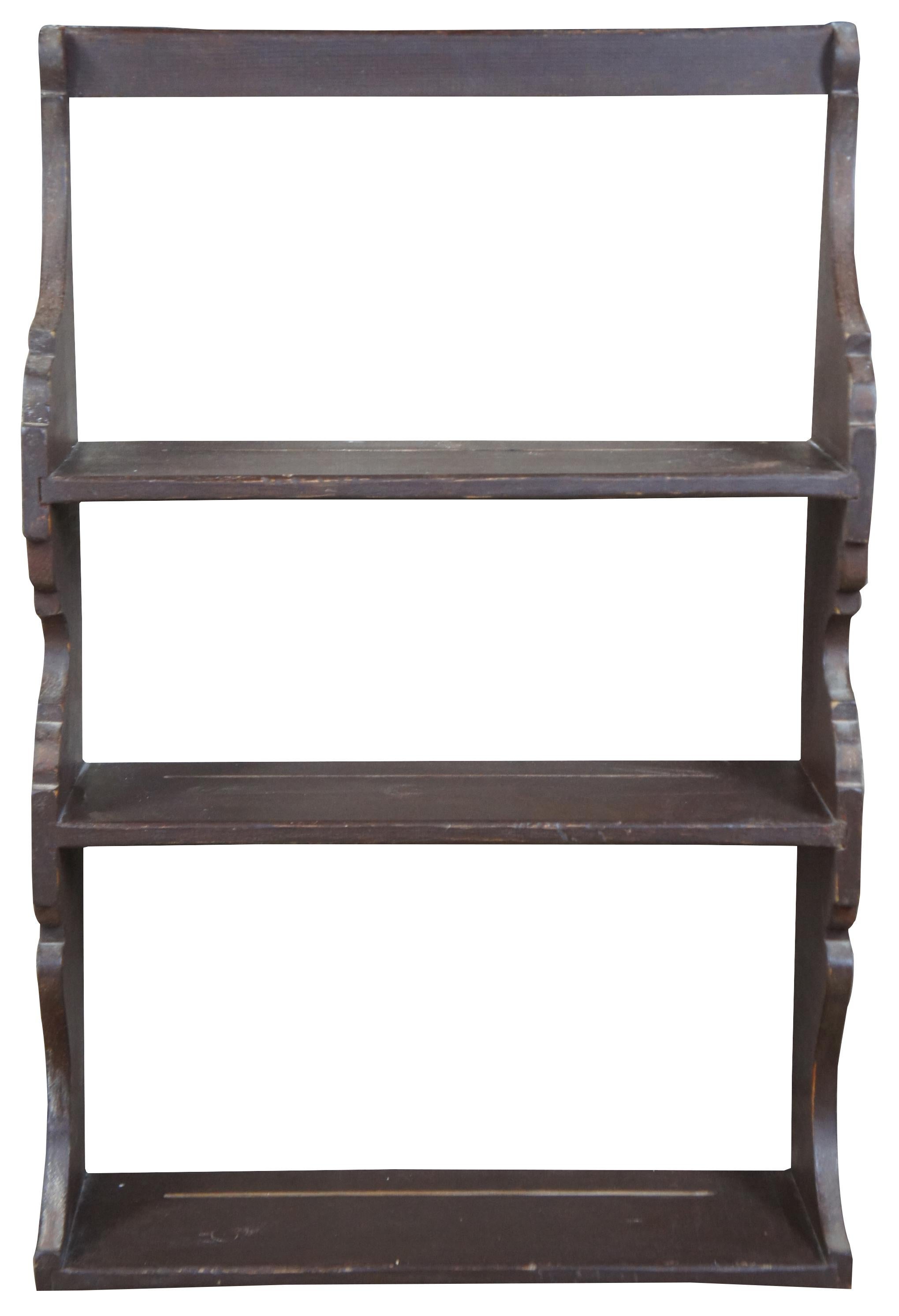 20th century pine hanging shelf. Features 3 shelves with a serpentine design along the sides. Includes grooves along the back for plate storage. Finished in brown paint.
  