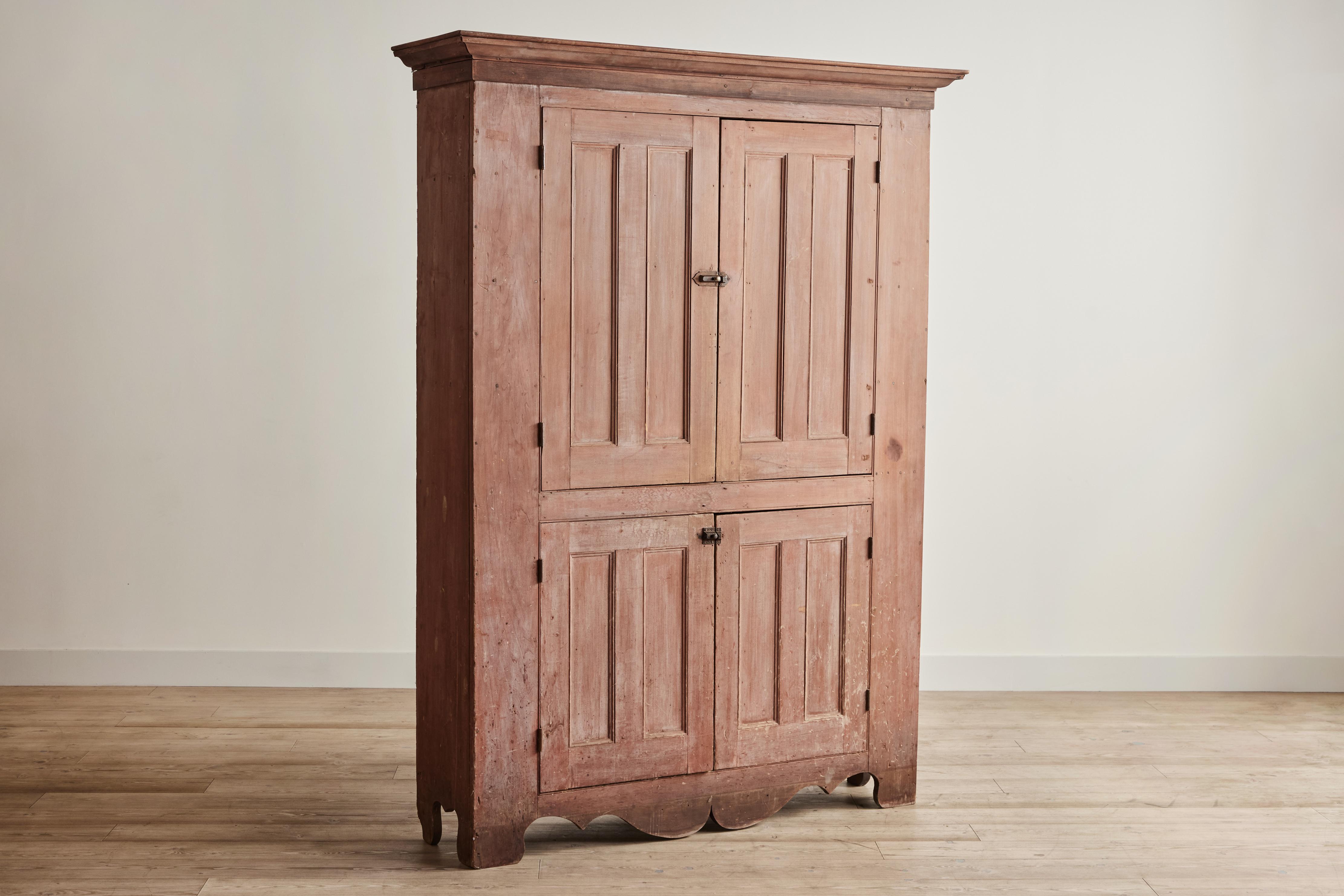Large early American wood cupboard painted a faint salmon color. Cabinet has two large compartments with interior shelving for storage. Wear throughout it consistent with age and use. 