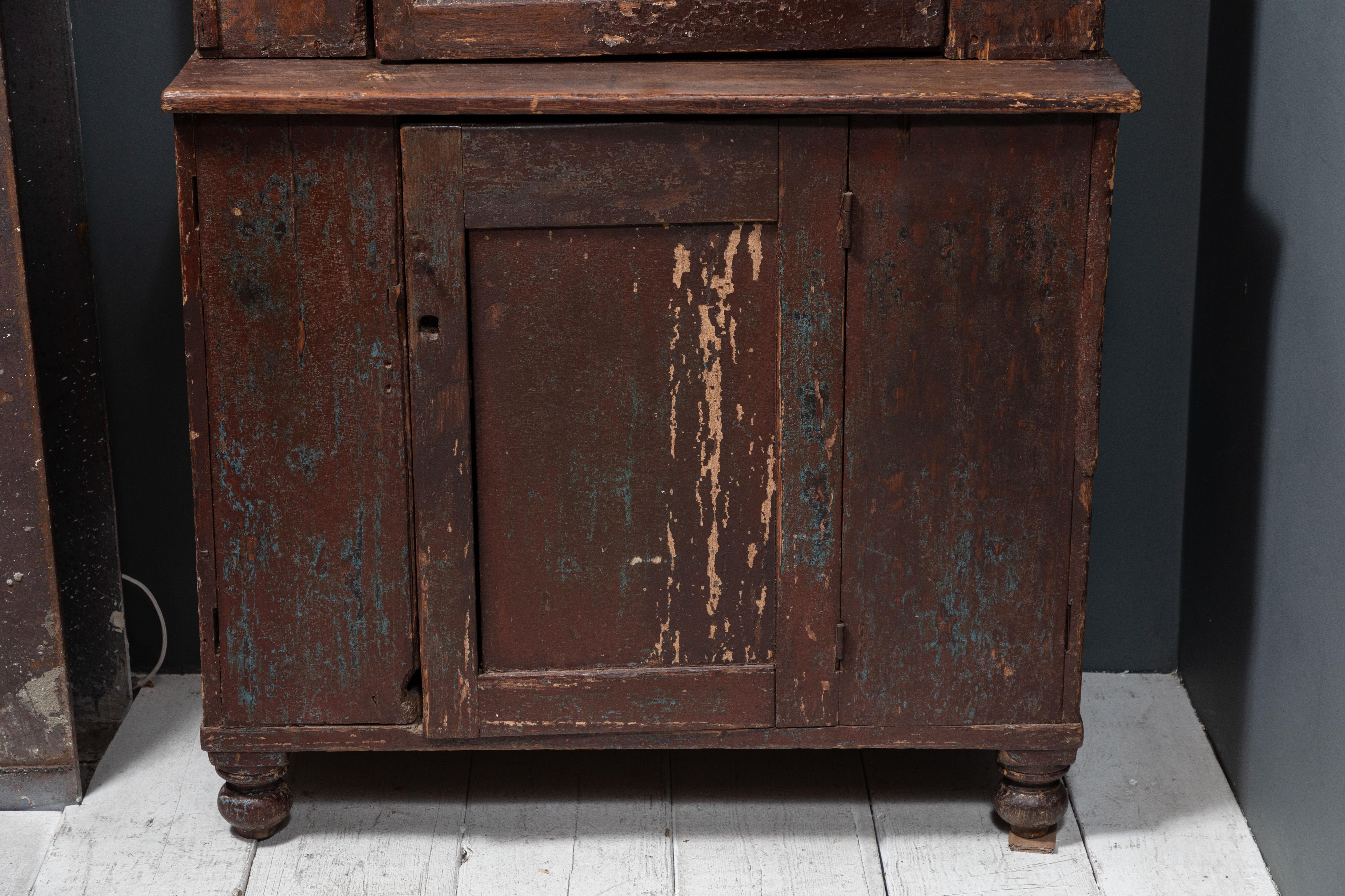 Rustic early American hutch. Upper four paned glass door with display shelves, lower door for closed storage. The hutch is finished with a crowned top and turned round feet.