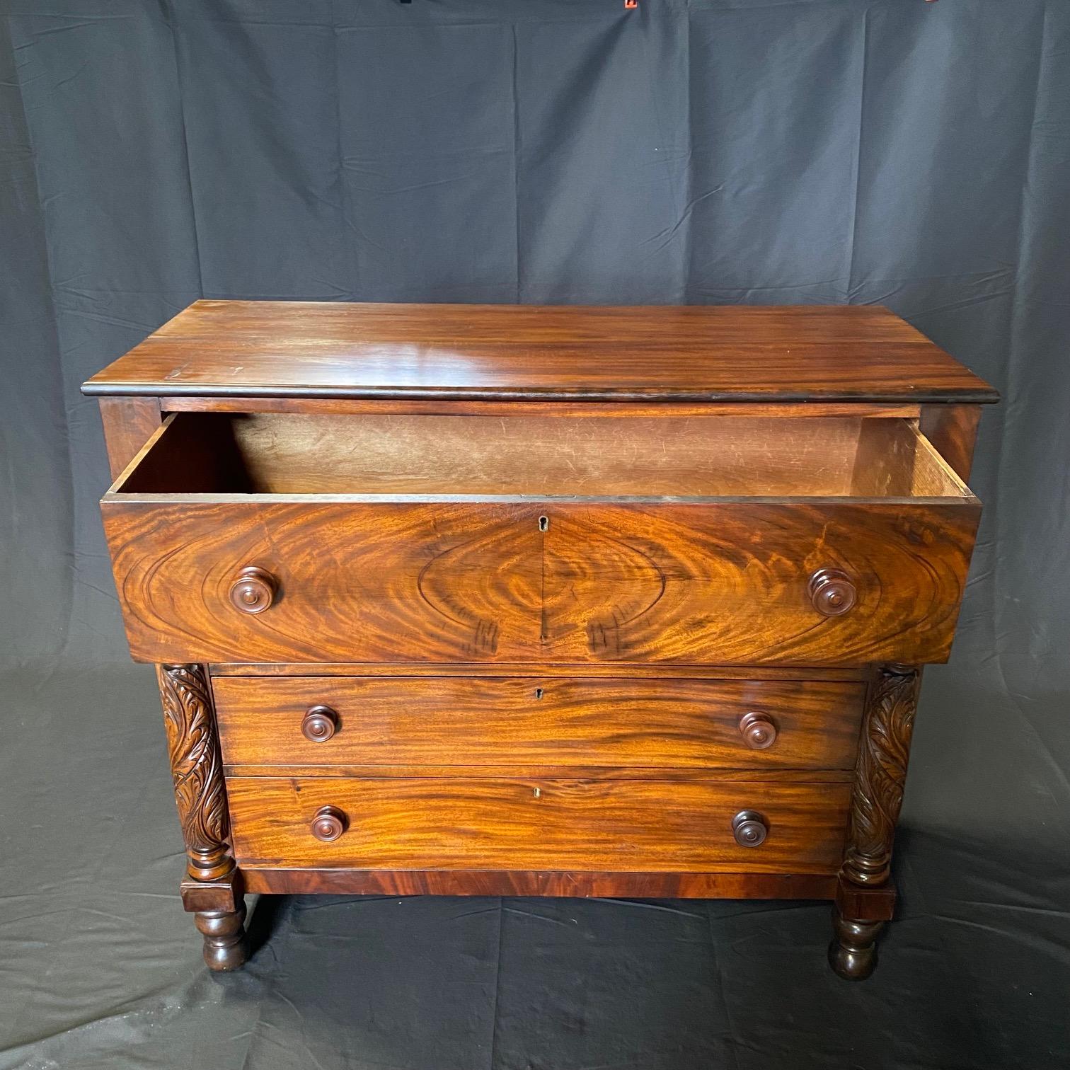 From the Federal period, a very beautiful American Neoclassical chest of drawers in fine bookmatched mahogany with one overhanging drawer supported on the sides by two beautifully turned and carved columns with acanthus leaves. Three more spacious