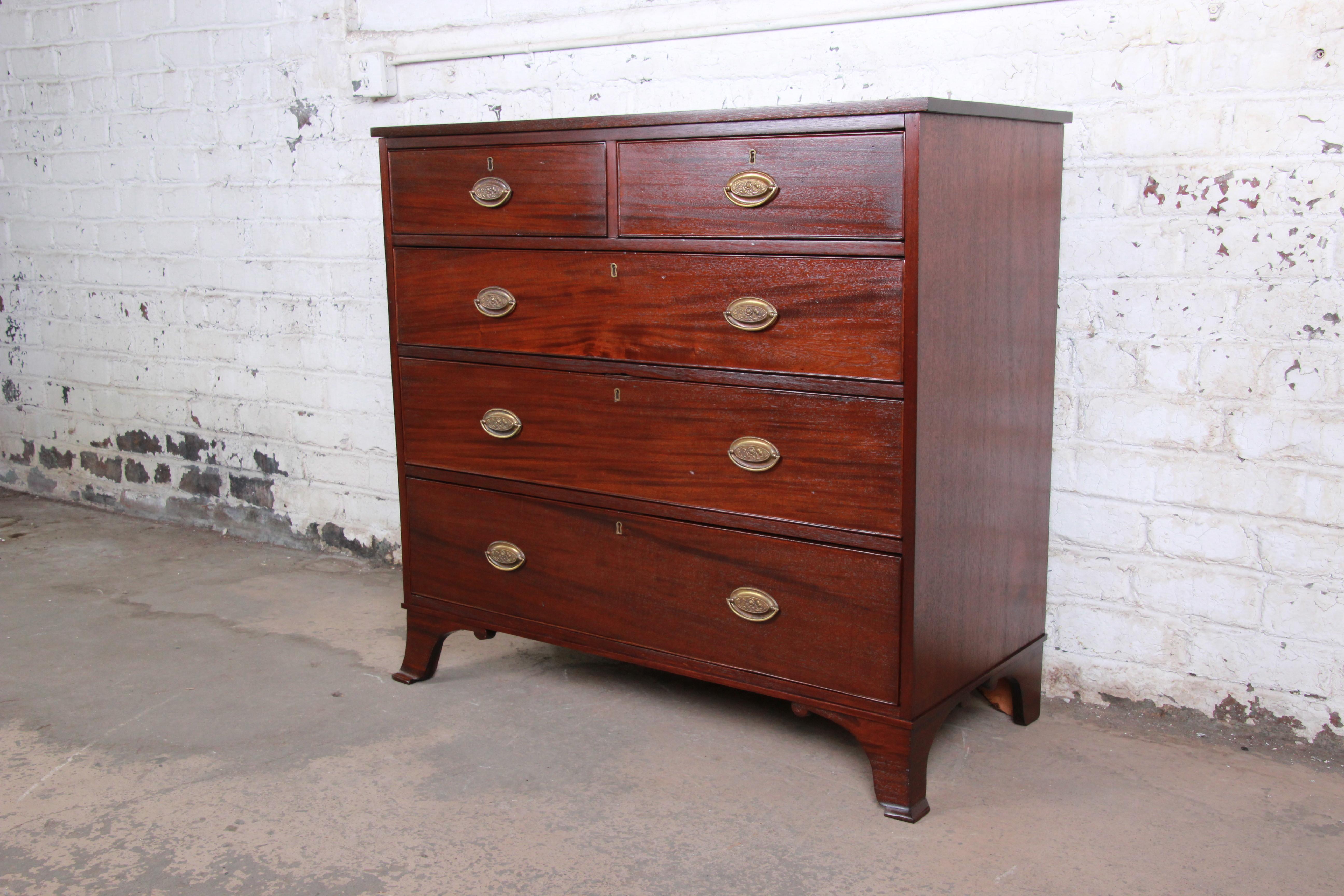 An exceptional 19th century early American mahogany chest of drawers. The dresser features solid mahogany construction with gorgeous wood grain and carved French feet. It offers ample storage, with five deep hand-carved dovetailed drawers. The