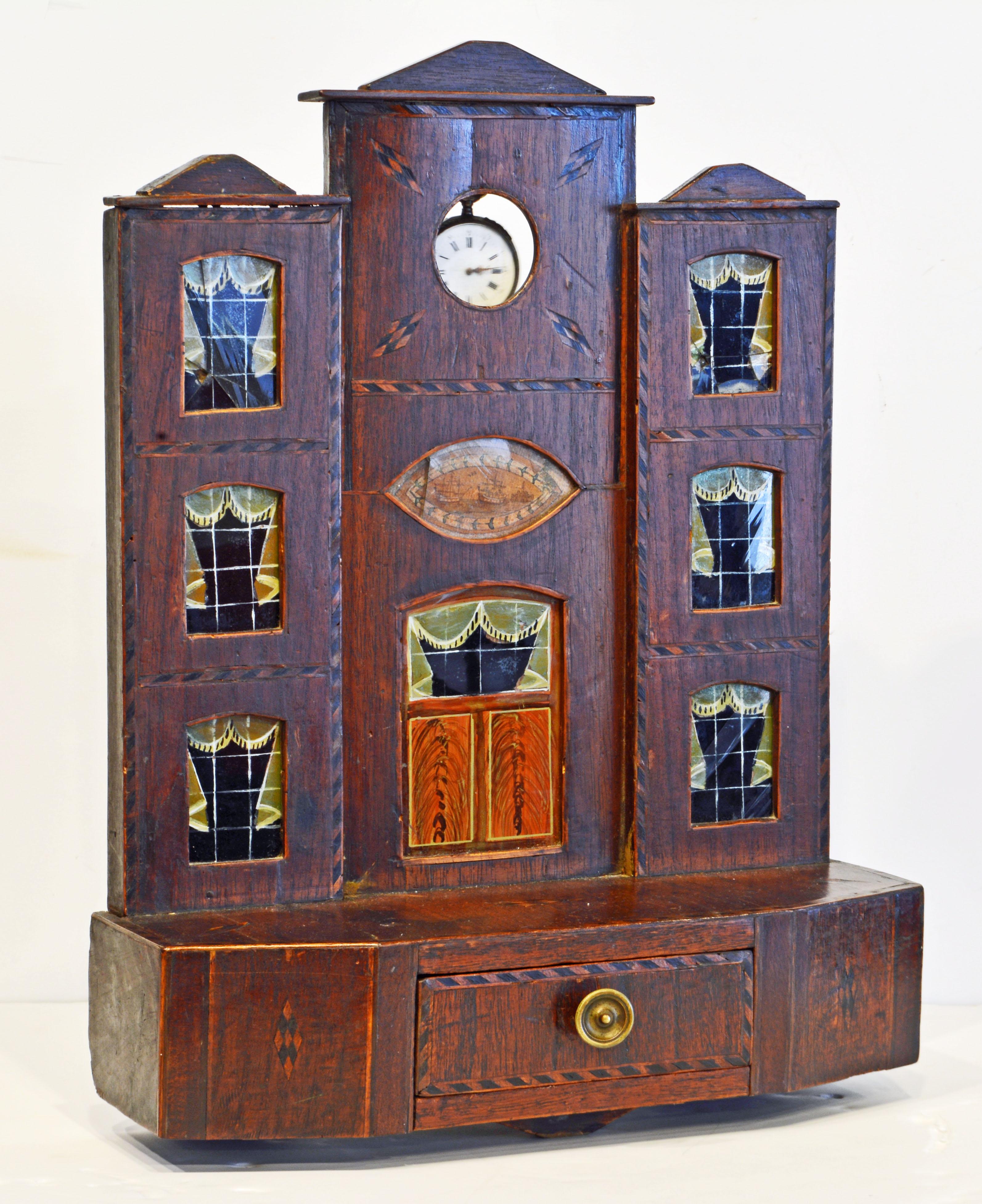 This early American inlaid pocket watch hutch or stand is made in the form of a three story house on a base with one drawer. The door and windows are made of glass painted on the backside. The piece is beautifully inlaid in a nautical theme and