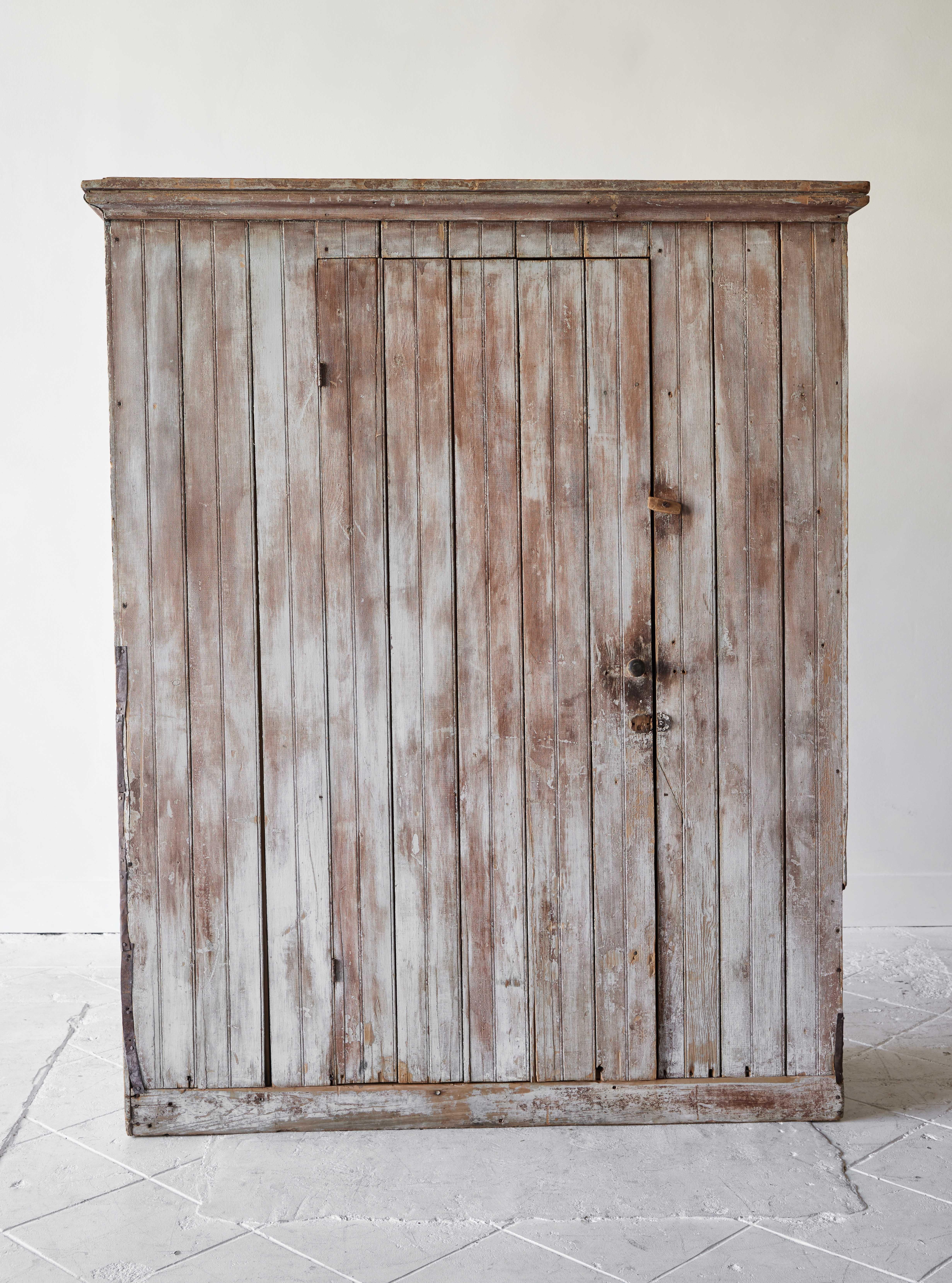 A very handsome rustic Early American single door cupboard painted gray with rust colored undertones. This cabinet is a wonderful utilitarian piece and features interior shelves and coat hooks on the interior door allowing room for ample storage.