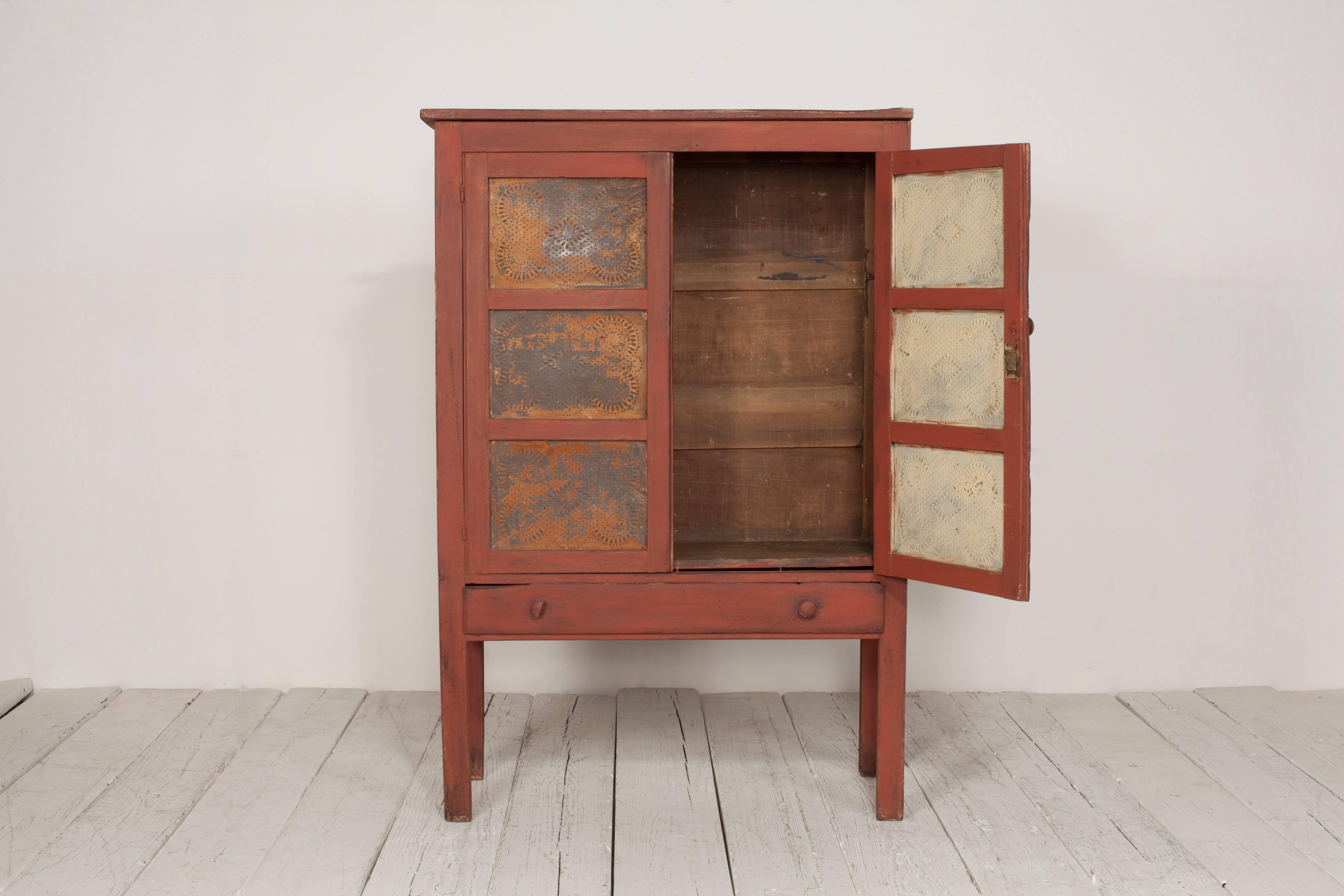 Early American terra cotta colored pie safe cabinet with patina metal details and single drawer.