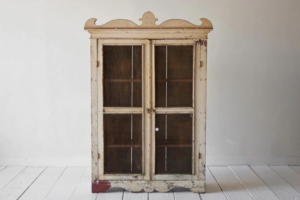 Early American pie safe cupboard painted red and white with a crested pediment. The front is enclosed by two metal screened doors. Three interior shelves provide ample space for storage or display.