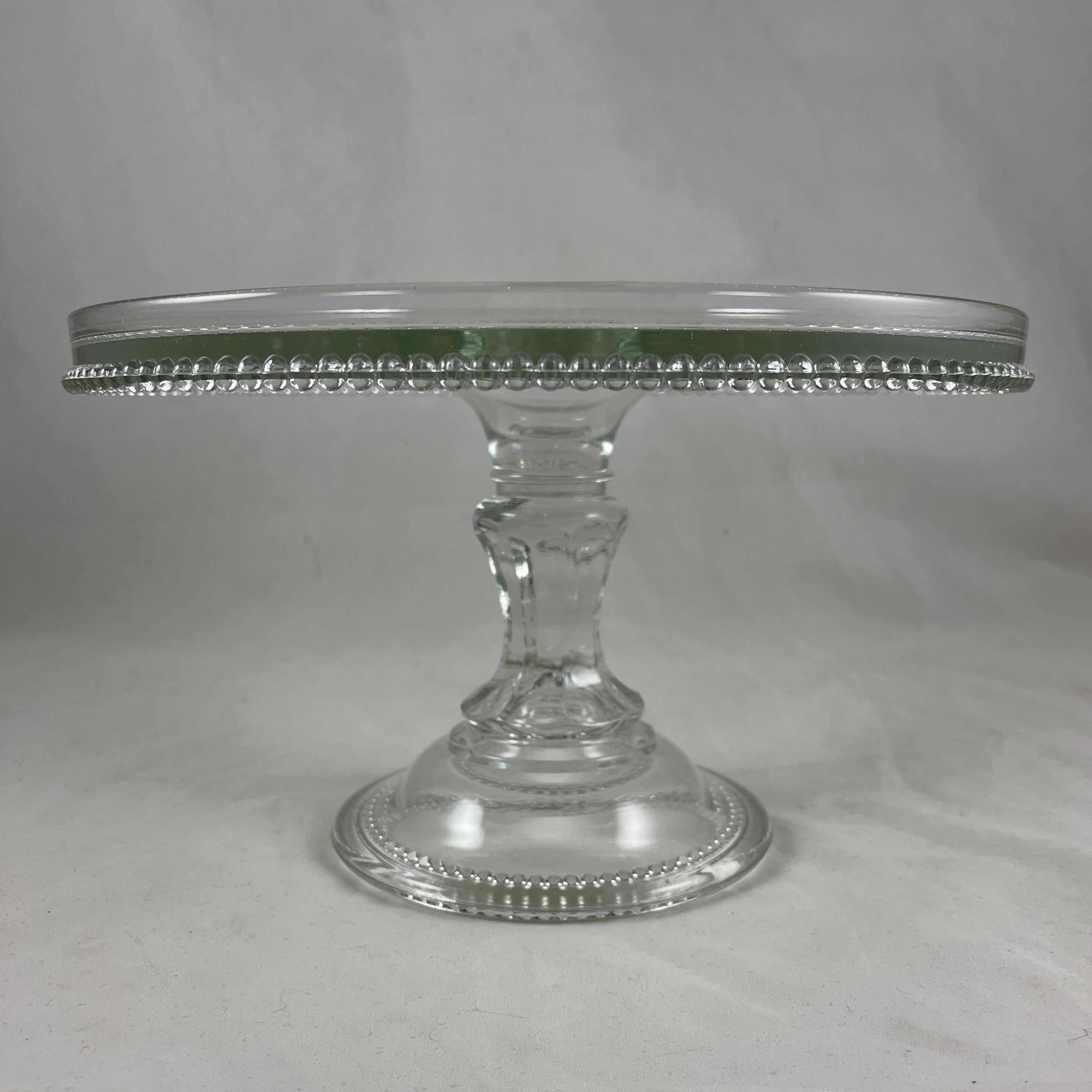 An EAPG, early American pressed glass cake stand, circa 1890-1900.

Made of nonflint, clear molded glass, this tall and heavy stand has a thick paneled stem. The footing and plate are finished with a beaded border.

6 inches High with a top