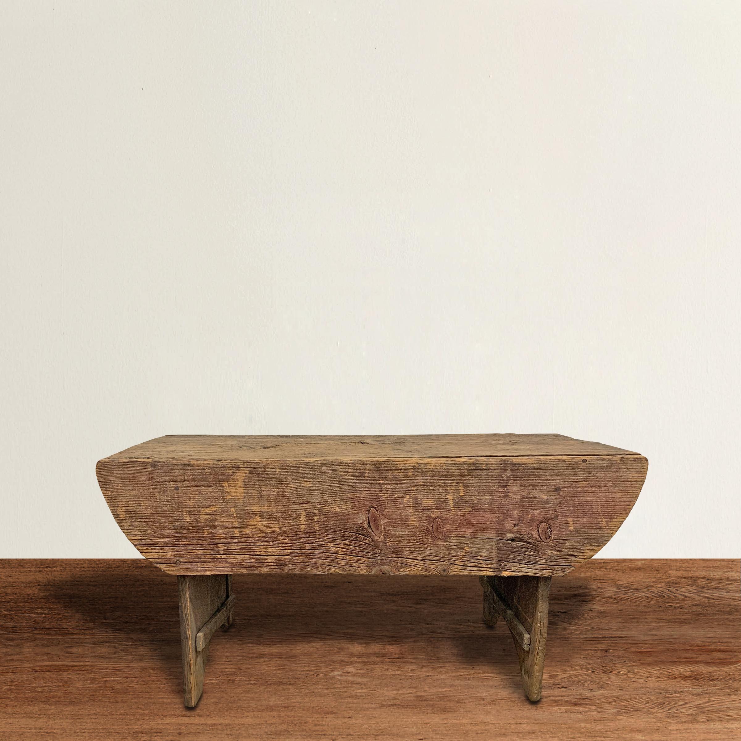A wonderful early 19th century American bench or low table of simple construction with a solid plank top and solid plank legs with semi-circular cutout. Bench retains some of its original red paint.