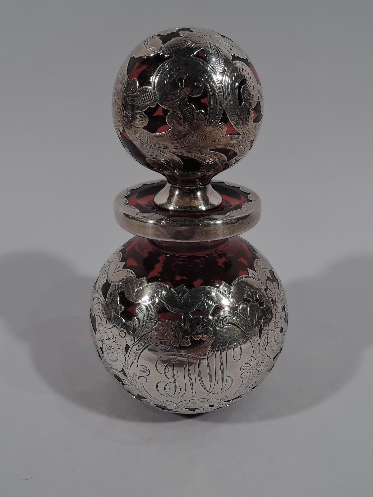 Early red glass silver overlay perfume. Made by Gorham in Providence, circa 1886. Globular with short neck and flat averted rim. Ball stopper. Dense and engraved overlay with scrolls and flowers. A concentrated design with small reveals of the