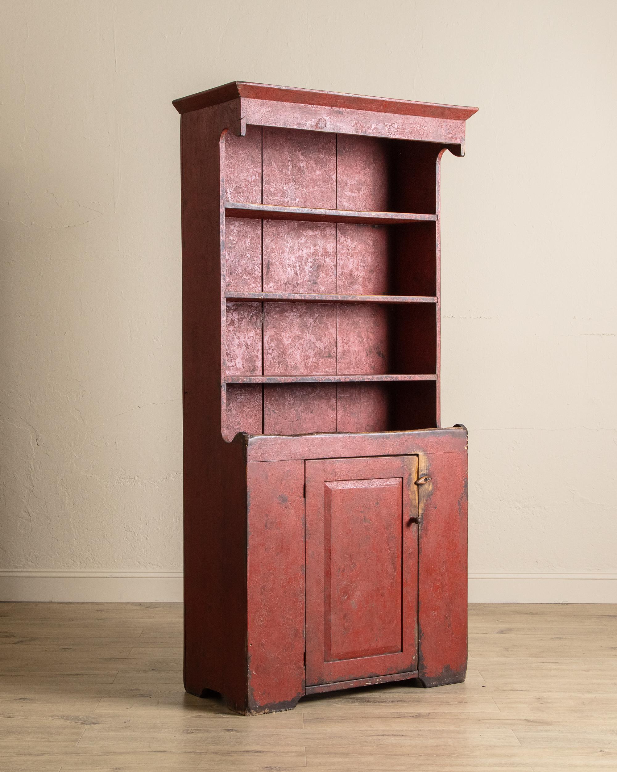 Cette armoire à dos d'âne datant du début du 19e siècle a conservé sa riche finition peinte rouge d'origine, magnifiquement vieillie pour révéler des couches d'histoire et de caractère. La partie supérieure comporte des étagères ouvertes, parfaites