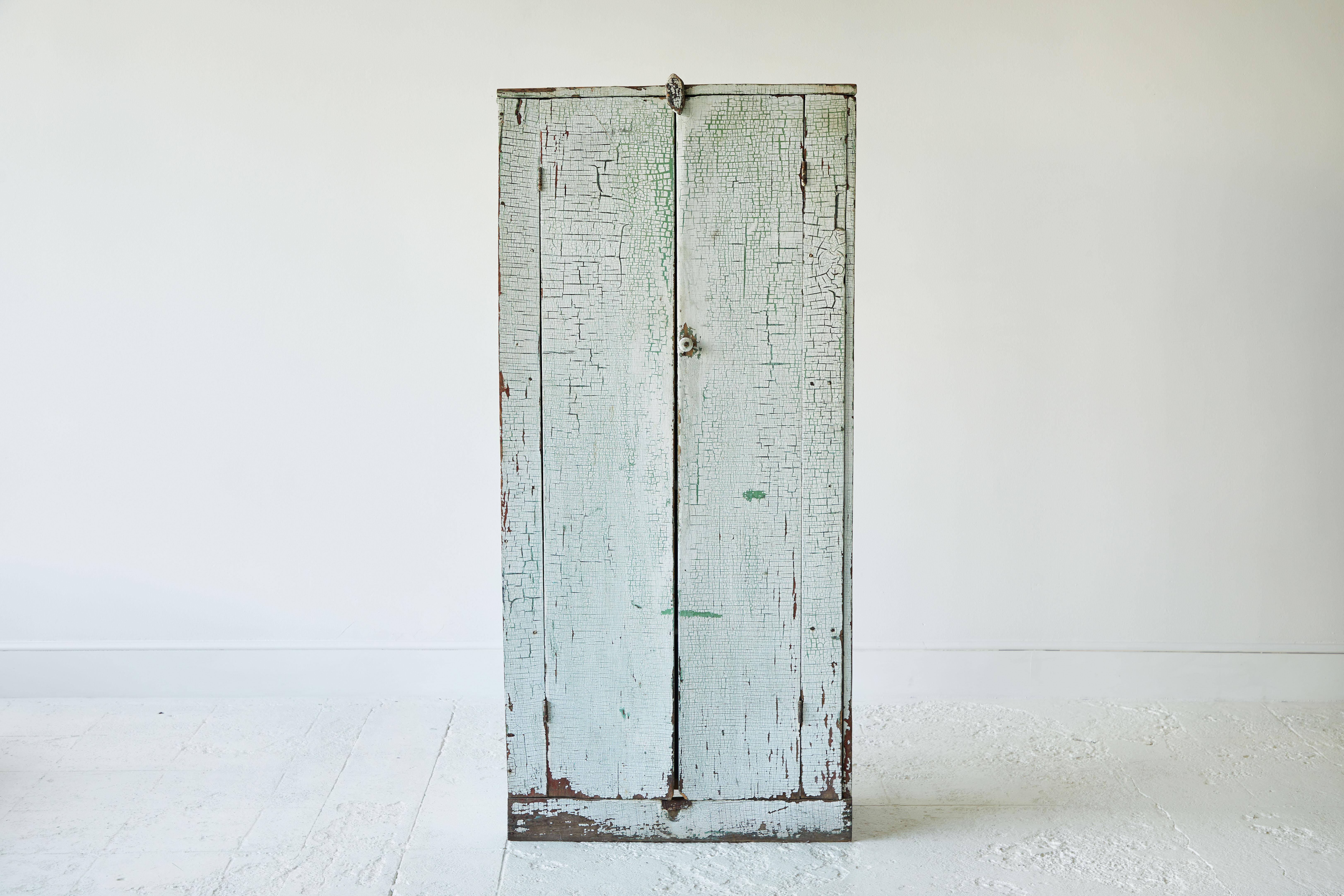 Early American rustic painted two-door cabinet with green undertones. The interior of the cabinet has four shelves.