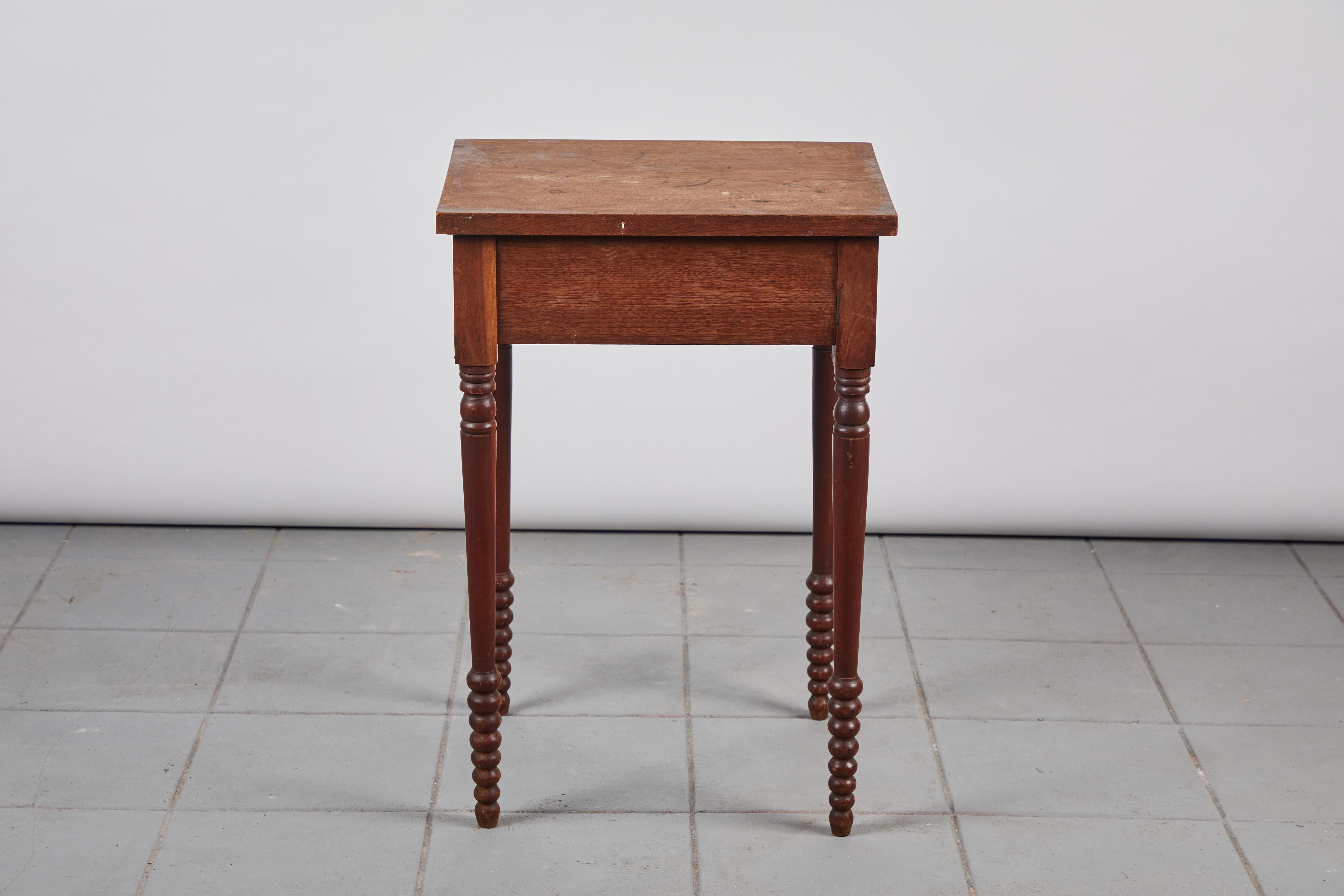 Early American rustic side table with turned legs and a single drawer.