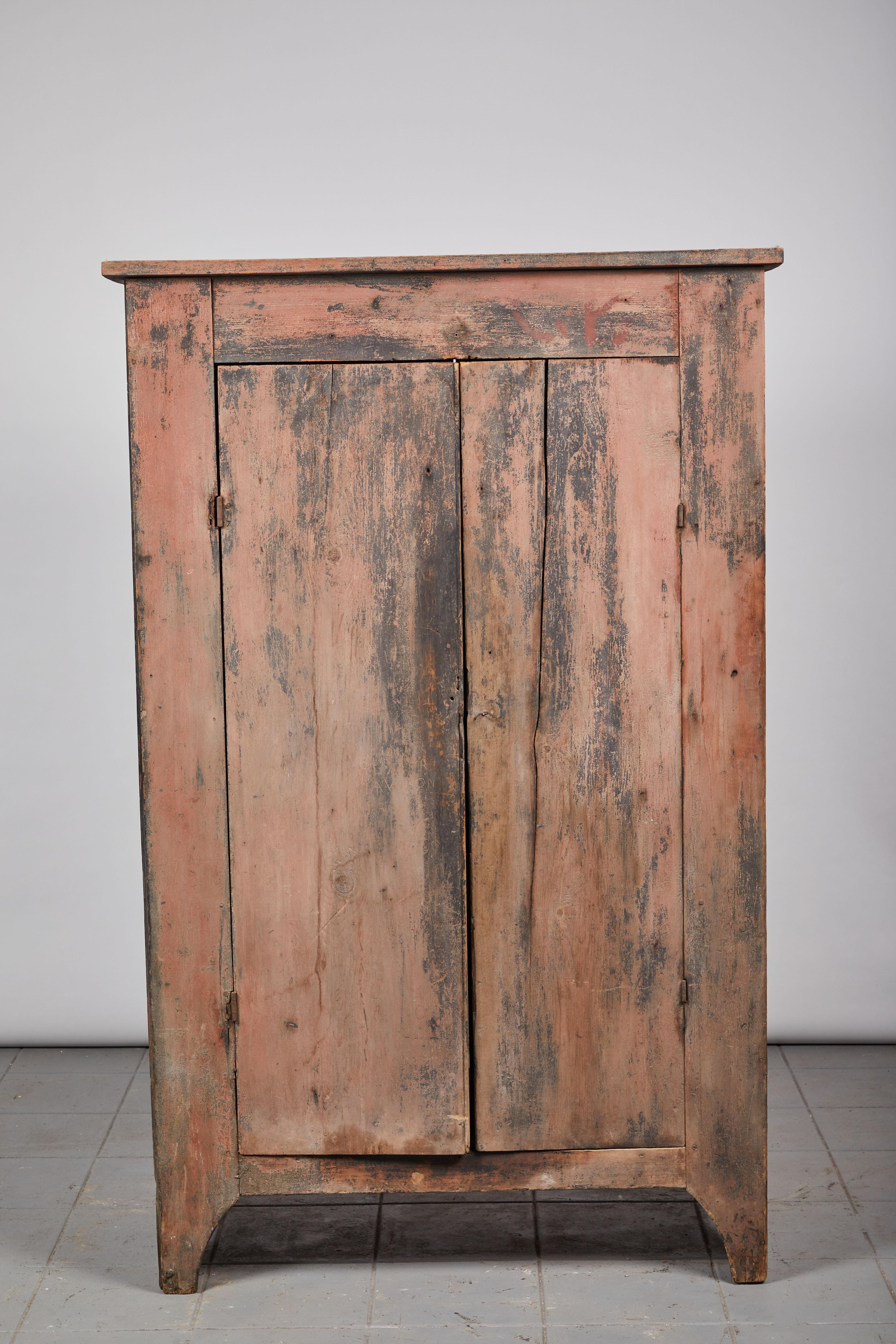 Early American rustic two-door cabinet painted with hues of pink and black. Interior consists of three shelves.