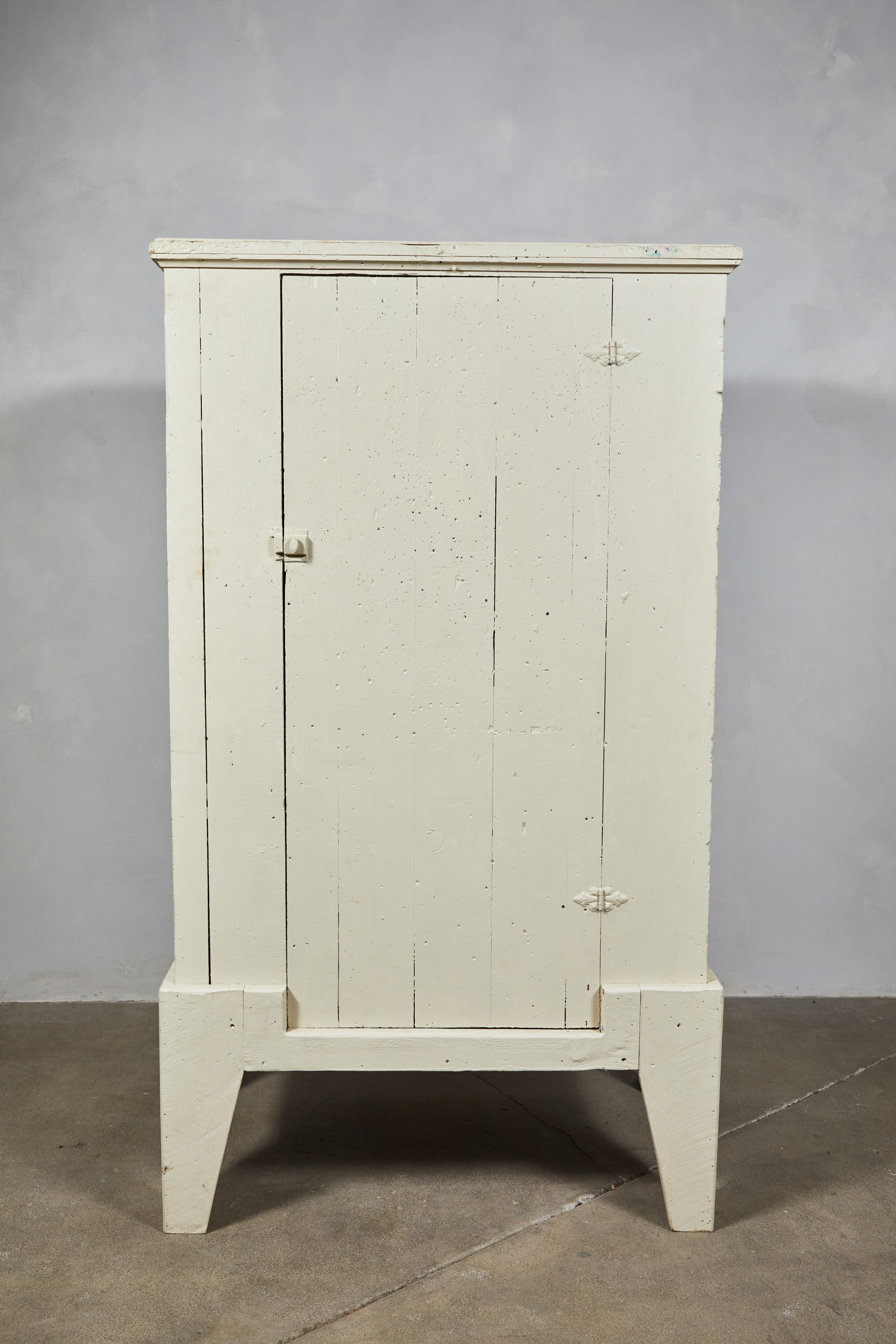 Early American white painted single door cabinet with chunky legs. Inside offers two shelves.