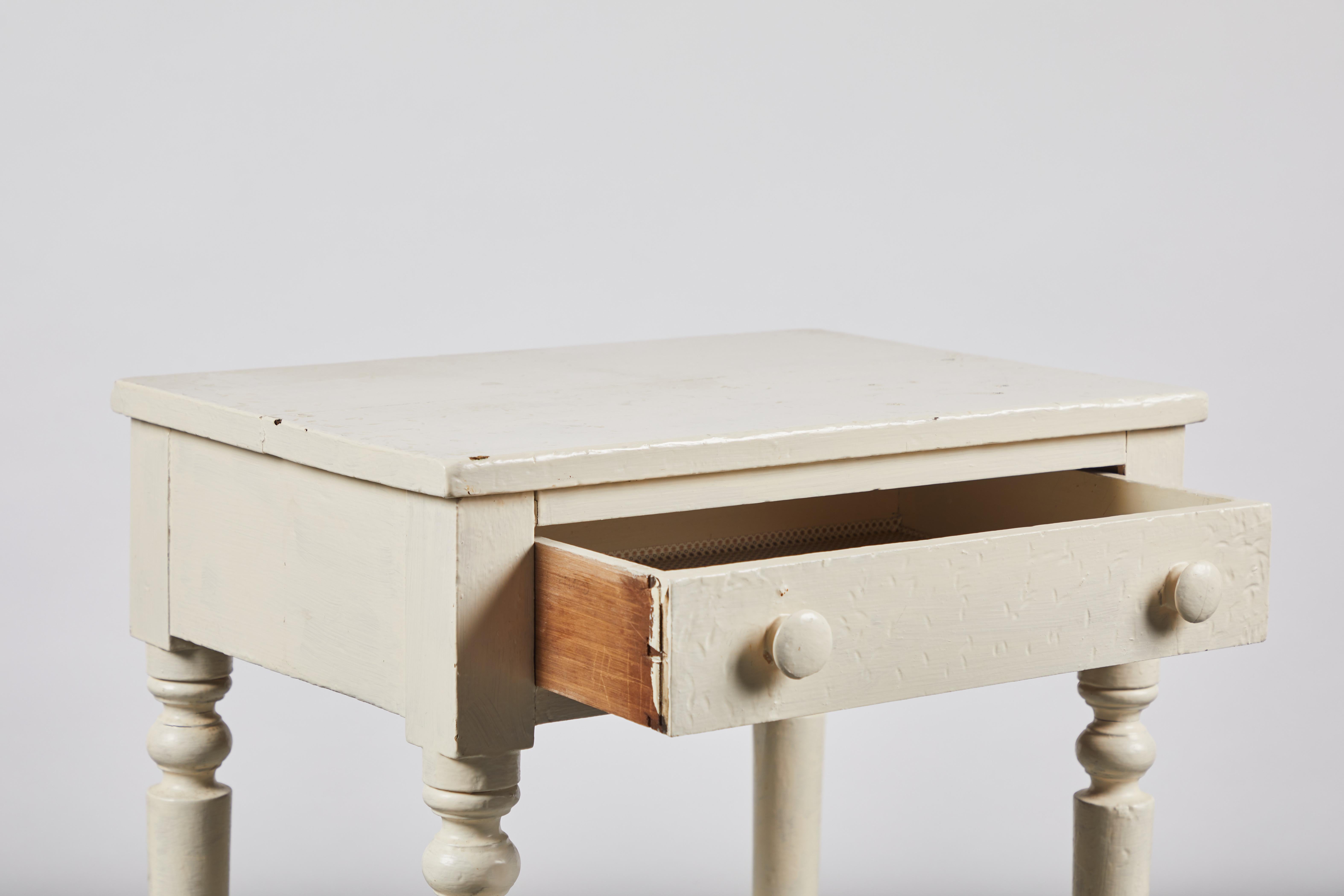 Early American white painted side table with turned legs and a single drawer.