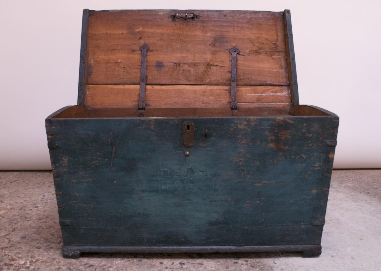 Primitive trunk / chest composed of a hinged wood plank top and painted wooden frame with brass and steel embellishments (brass nailheads with hand-hammered steel handles / hinges / locking mechanism, which is no longer operational) circa 18th