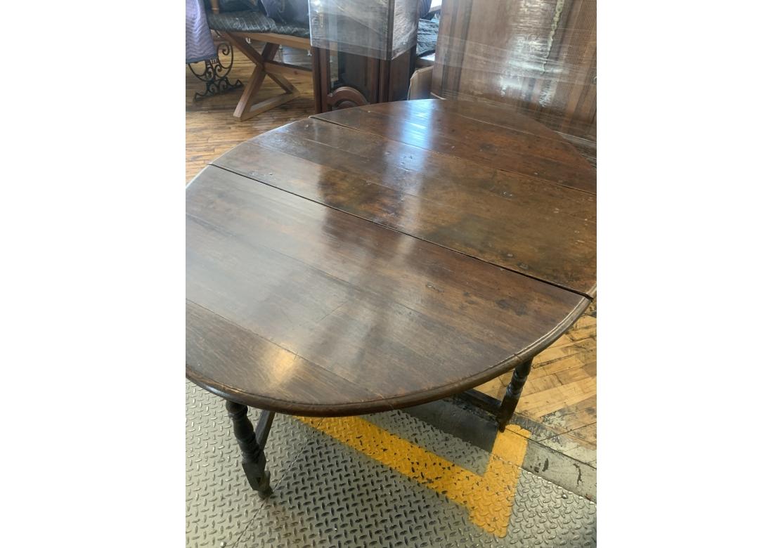 An early timeworn  and likely English Antique Gate leg oak table.  With two demilune form drop leaves, one on either end. The table has six feet with four feet and stretcher supports with turned legs and two legs can swing out to support the leaves