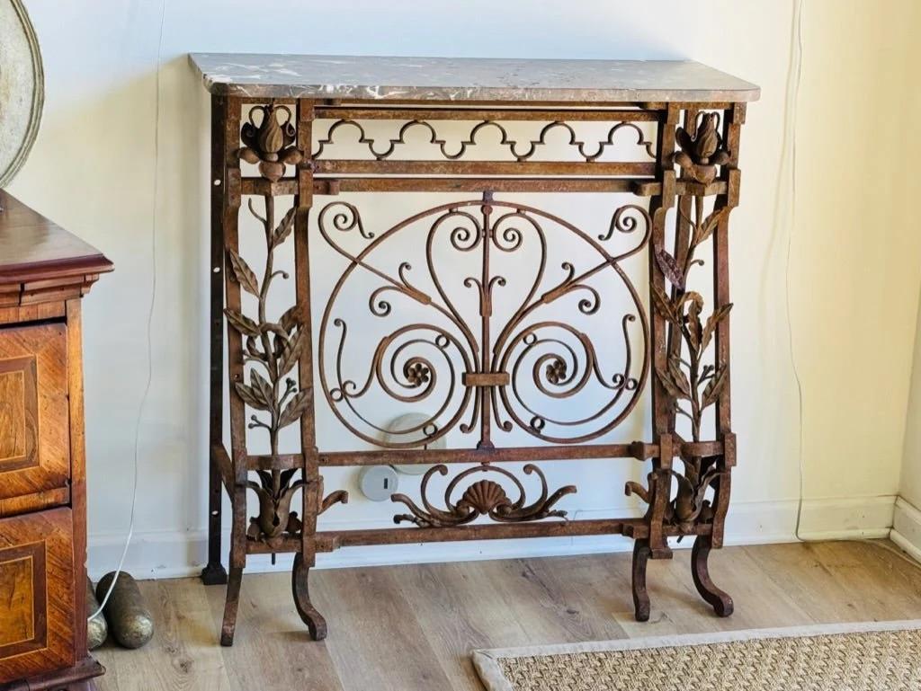 Early and finely wrought French Iron console, 19th C., having a marble top over a highly detailed base featuring vines and flowers flanking a central panel having a shell motif. 38.5” h. x 37.25” w. x 14.5” d.

