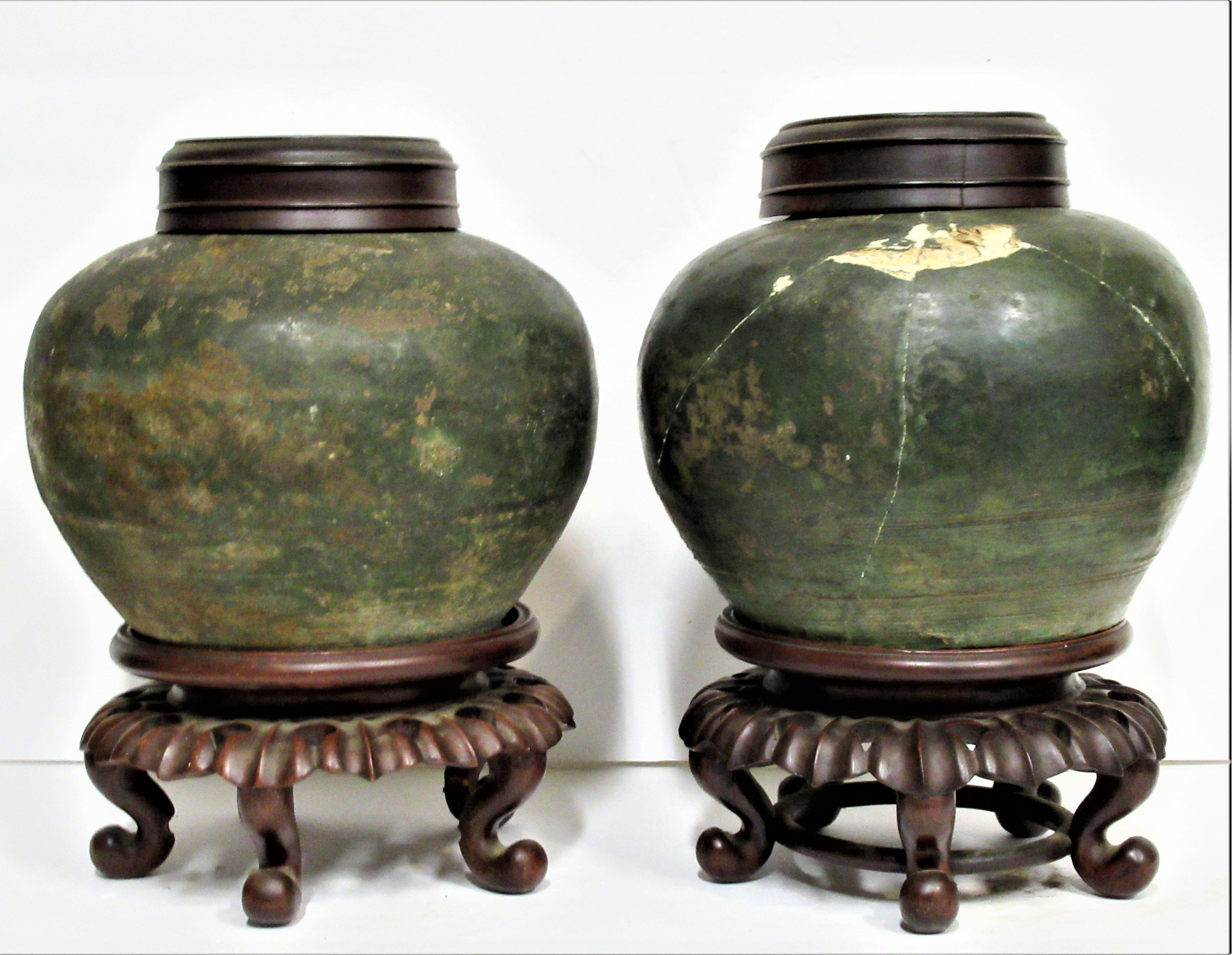 Pair of early Chinese ceramic tea jars with beautifully aged glazed surface color and archaic form. The carved wooden bases look to be 19th century. We think the jars are considerably older, and could date anywhere from 15th century - 18th century.