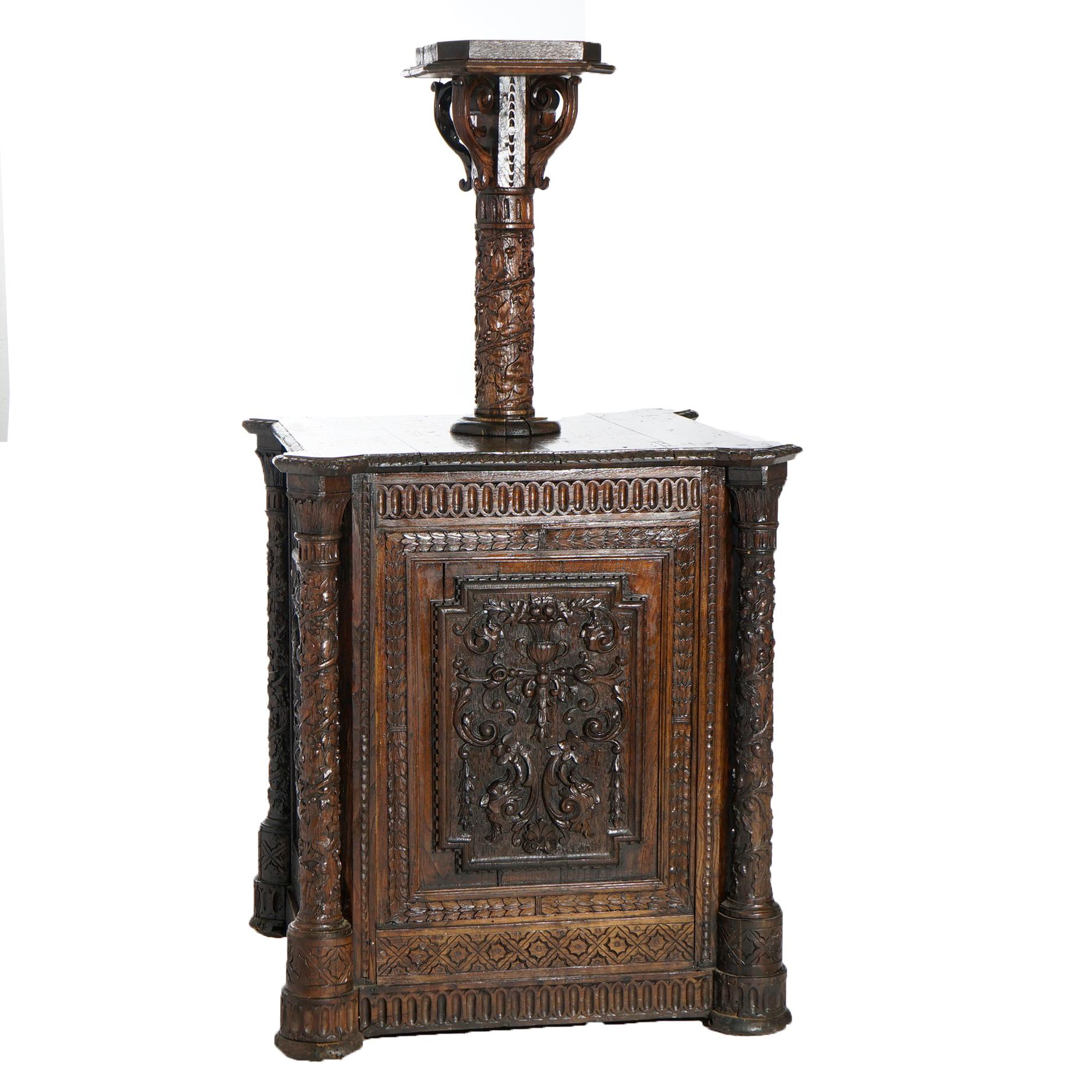 An early antique Continental reliquary cabinet offers deeply carved oak construction with central foliate column having square display with acanthus form corbels over single door cabinet base with carved flower urn, foliate and scroll carvings