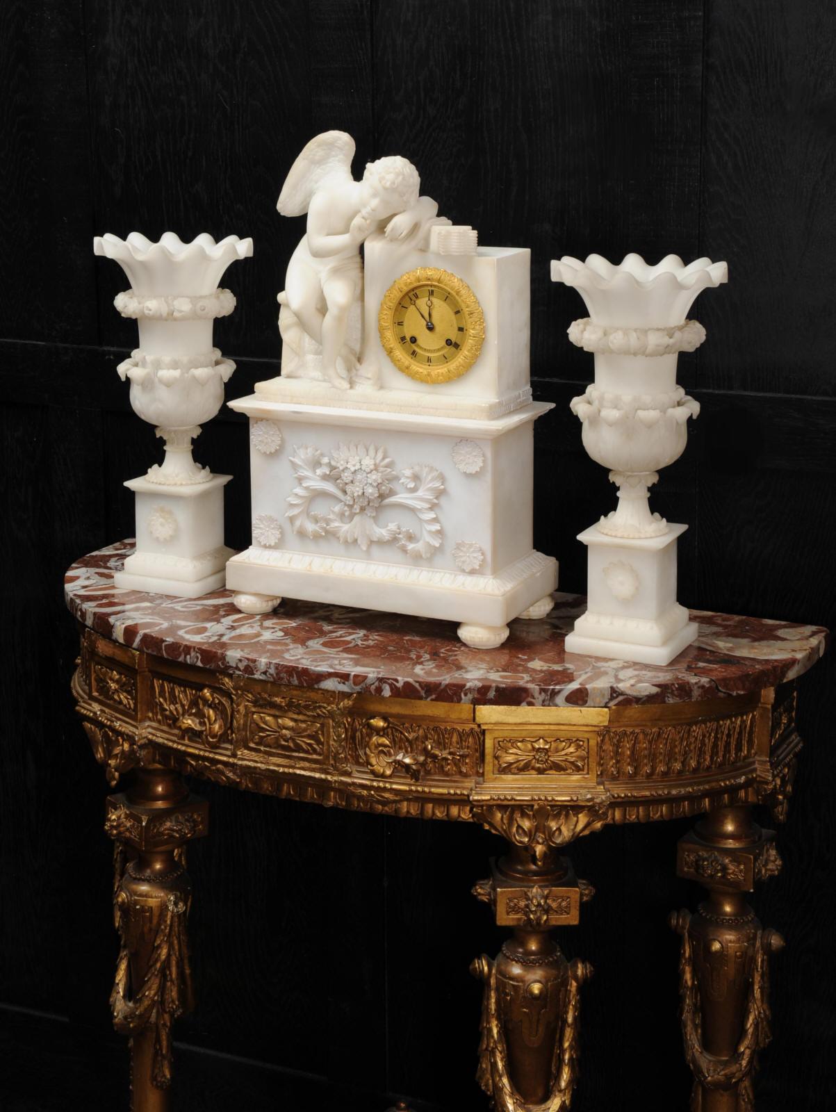 An early and stunning clock set, circa 1820, featuring a charming figure of Cupid, L’Amour Menaçant (Menacing Love) after the famous sculpture by Falconet currently in the Louvre. It is beautifully carved from crisp white alabaster, Cupid leans on
