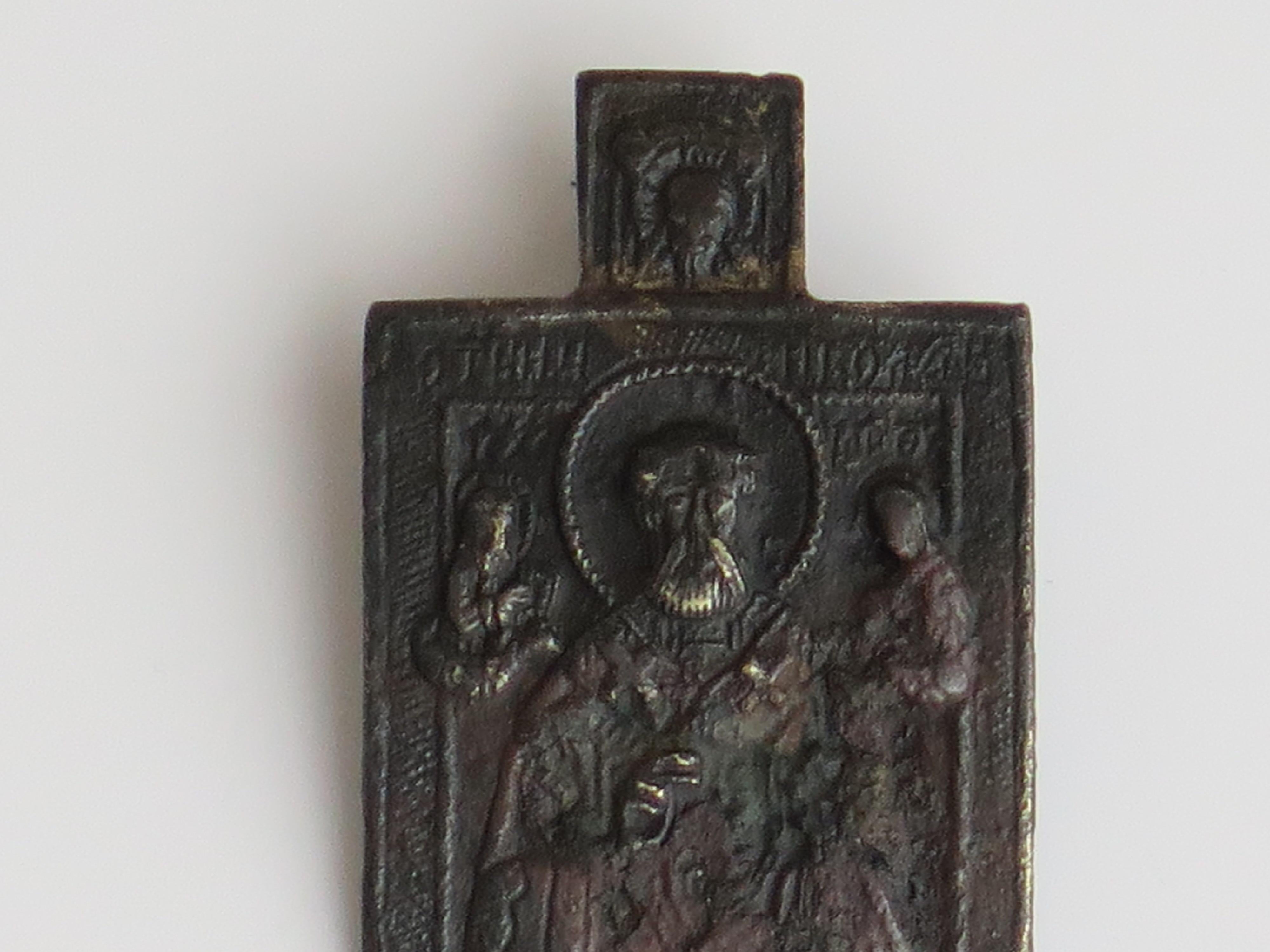 This is an early Russian orthodox travelling Icon, hand made of bronze, which we date to 18th Century or earlier. 

The bronze icon is cast with a main rectangular slightly curved shape with a smaller rectangular tab section above. The reverse has a