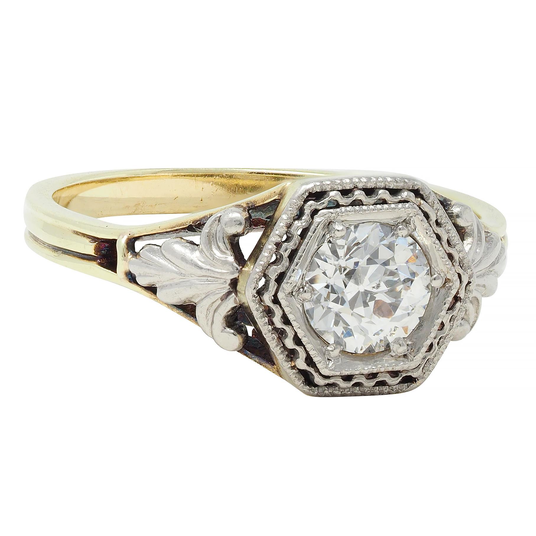 Centering an old European cut diamond weighing approximately 0.51 carat total - H color with SI2 clarity
Bead set in a platinum-topped hexagonal form head with squiggle motif filigree halo 
Planked by pierced platinum foliate motif appliqué