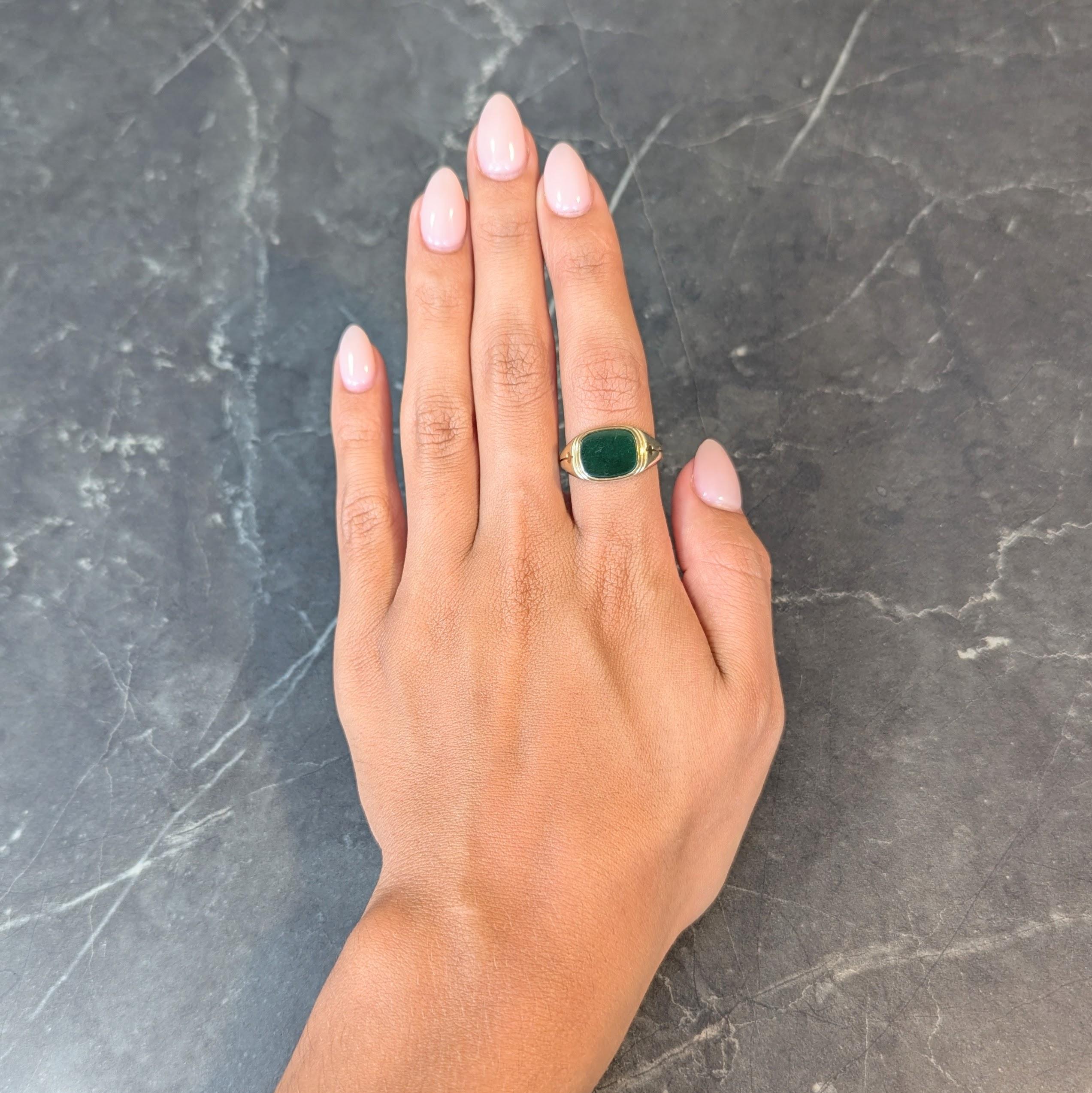 Centering a cushion-shaped nephrite jade tablet measuring 9.5 x 12.0 mm 
Translucent dark mossy green in color and bezel set
With a grooved surround and geometric shoulders
Tested as 14 karat gold
Circa: 1920s
Ring Size: 9 and sizable
Measures north