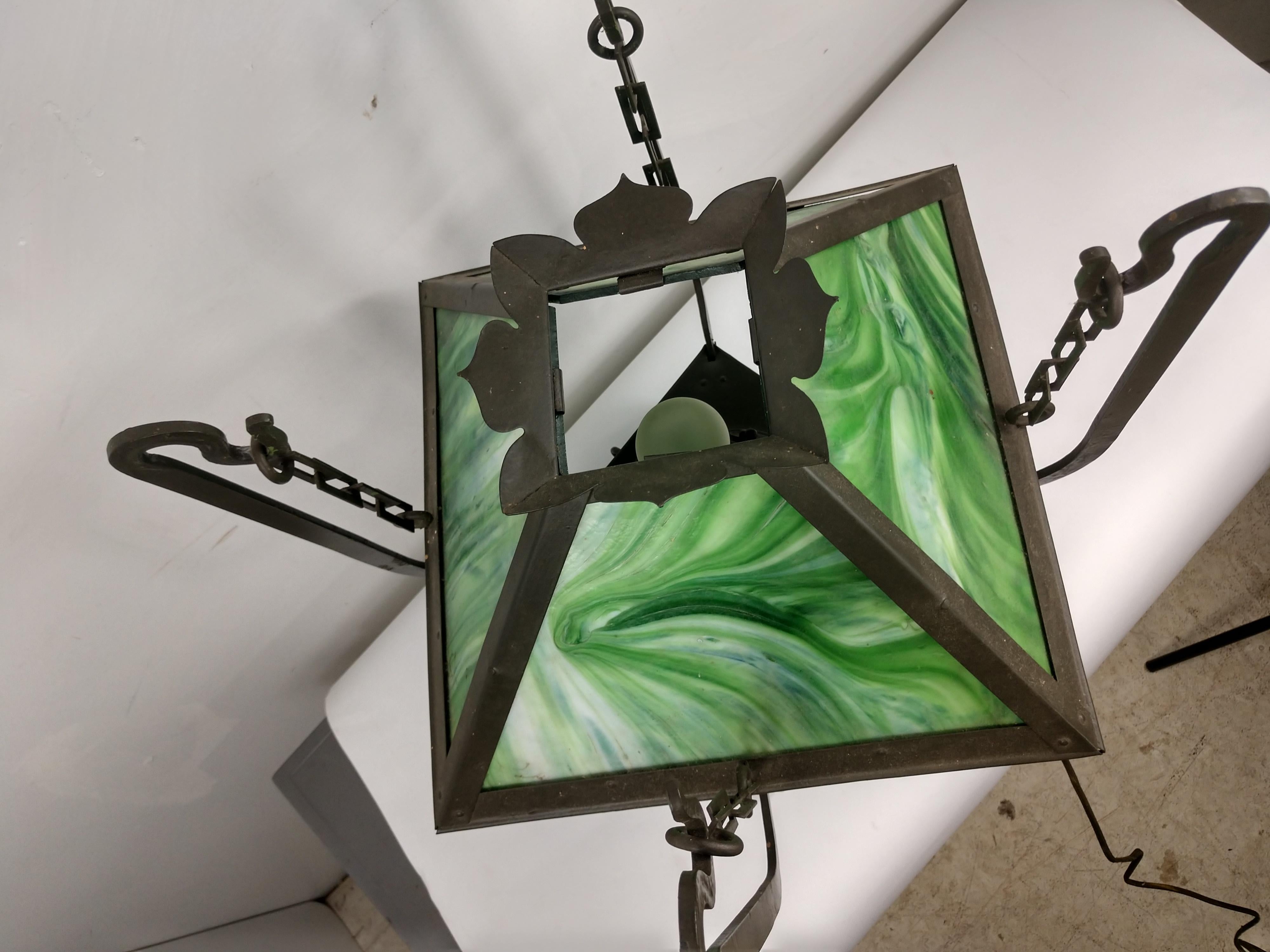 Great example from the arts & crafts period. A gas lamp by Miller which has been converted to electric. Beautiful green slag glass panels which is suspended by chain from the iron frame.
Lamp was most likely restored at some point and looks