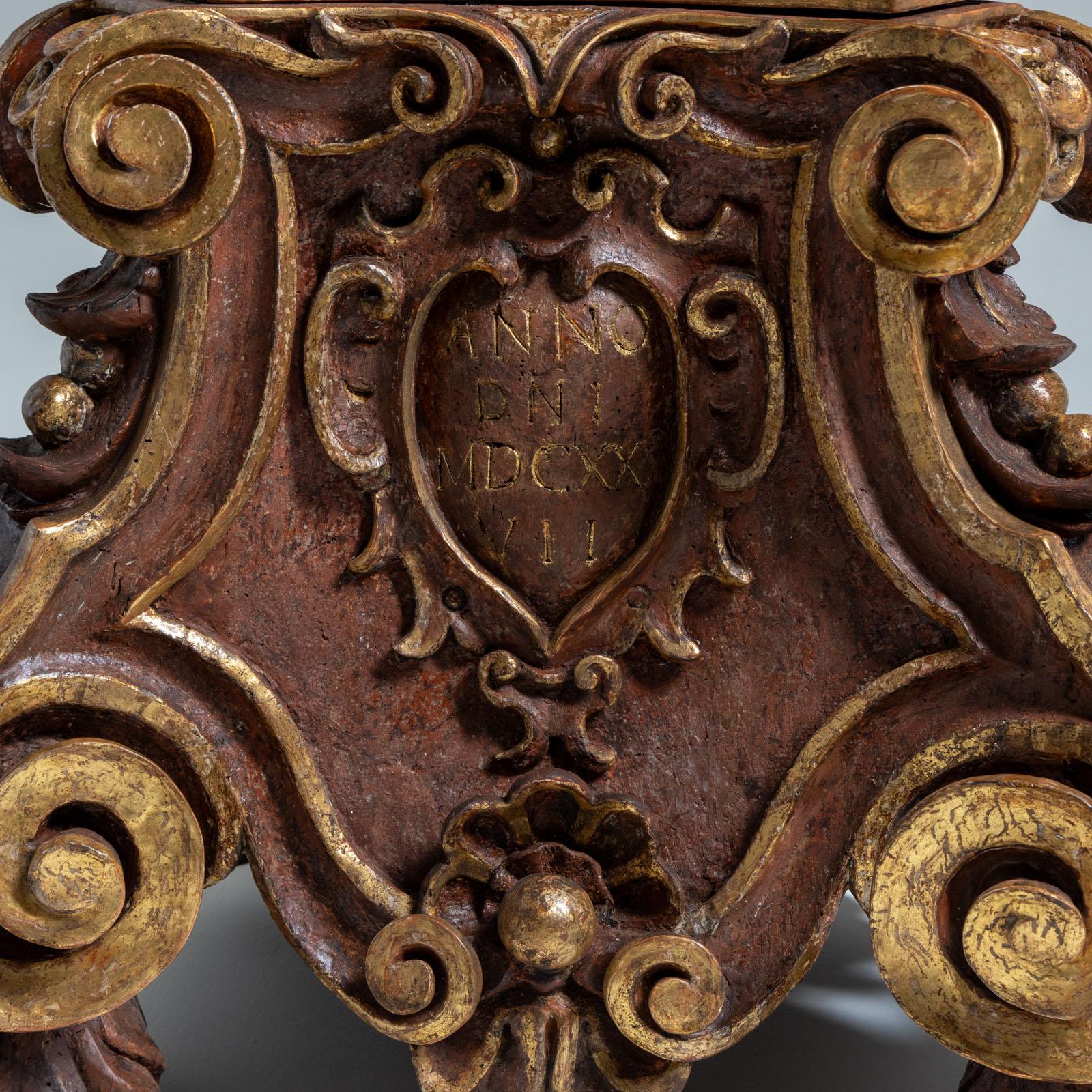 A pair of large altar candlesticks made of carved wood, partly with a gold patina and partly with a porphyry look, on a trefoil base with lion's paws and rocaille decoration. There are three coat of arms cartouches with a relief Annunciation scene