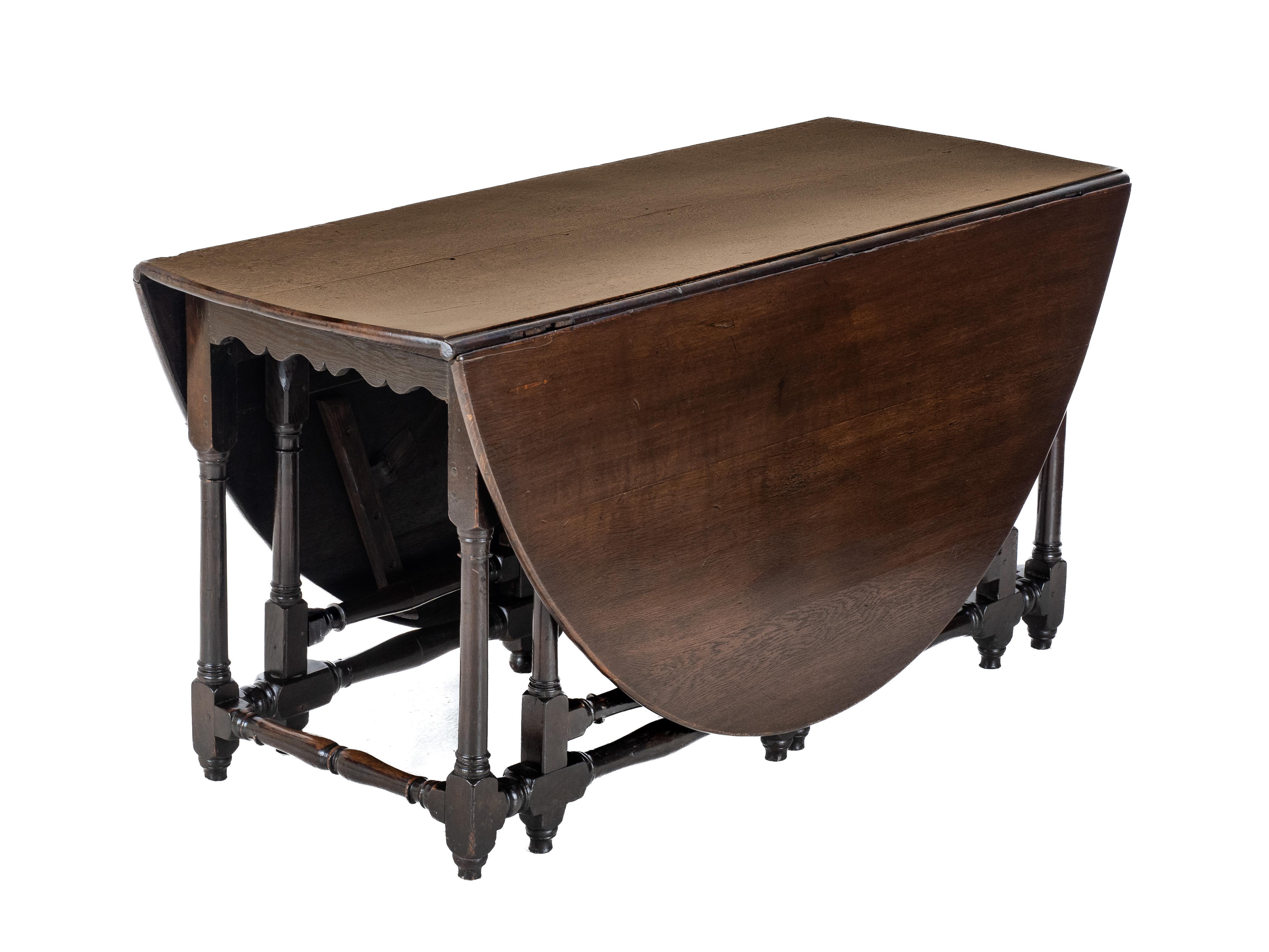 An early c.18th, oak gateleg dining table. Featuring solid oak construction throughout. Oval shaped, quality oak top, the drop leaves are supported by double gatelegs on each side. The substructure consists of scalloped frieze to both ends, turned