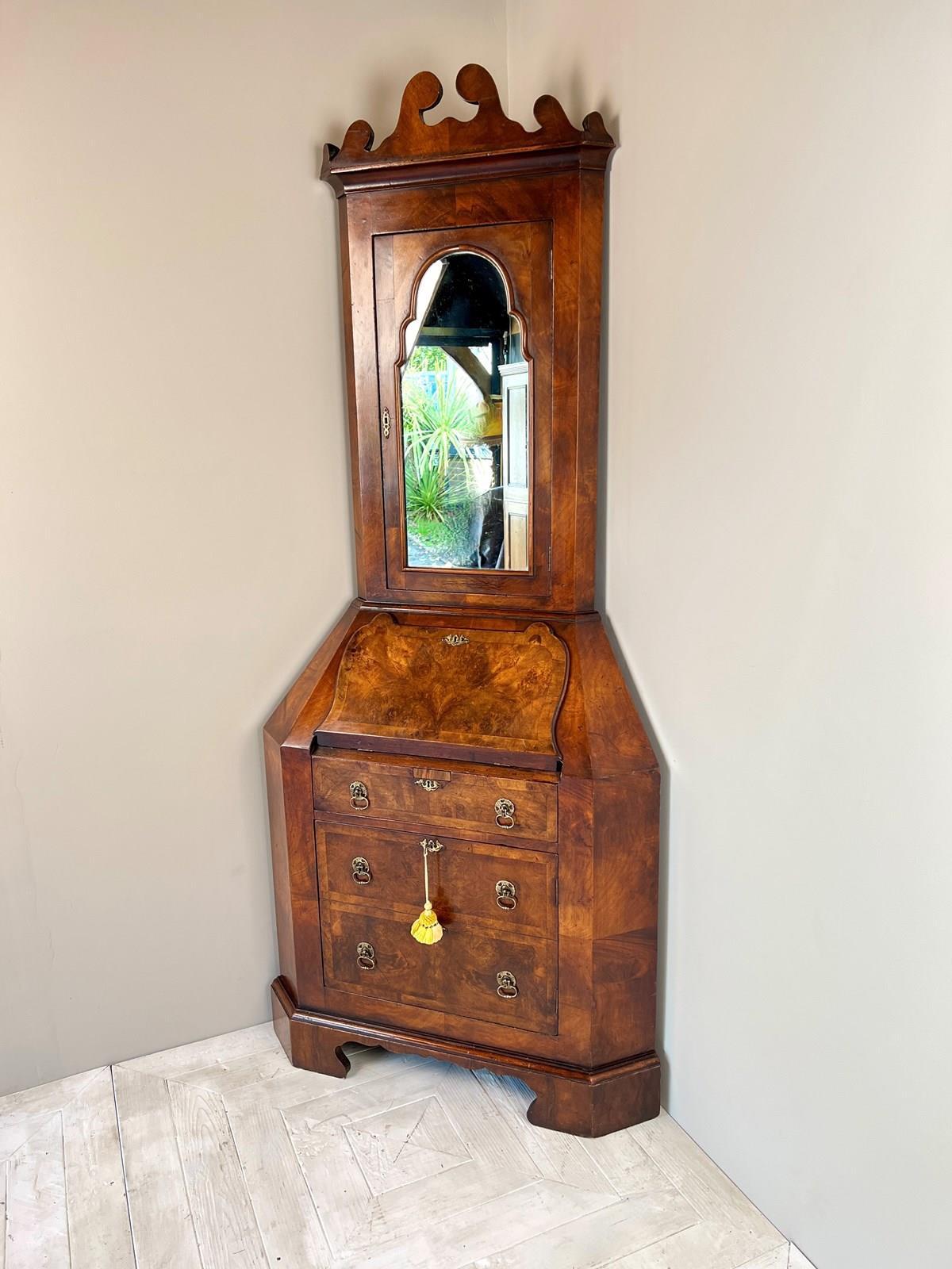A Good Example Early C20th Walnut Corner Bureau Bookcase in the Georgian Taste. The swan neck pediment above a mirrored door enclosing a cupboard with three shelves. The lower section of flared form with fall front bureau with fitted interior of