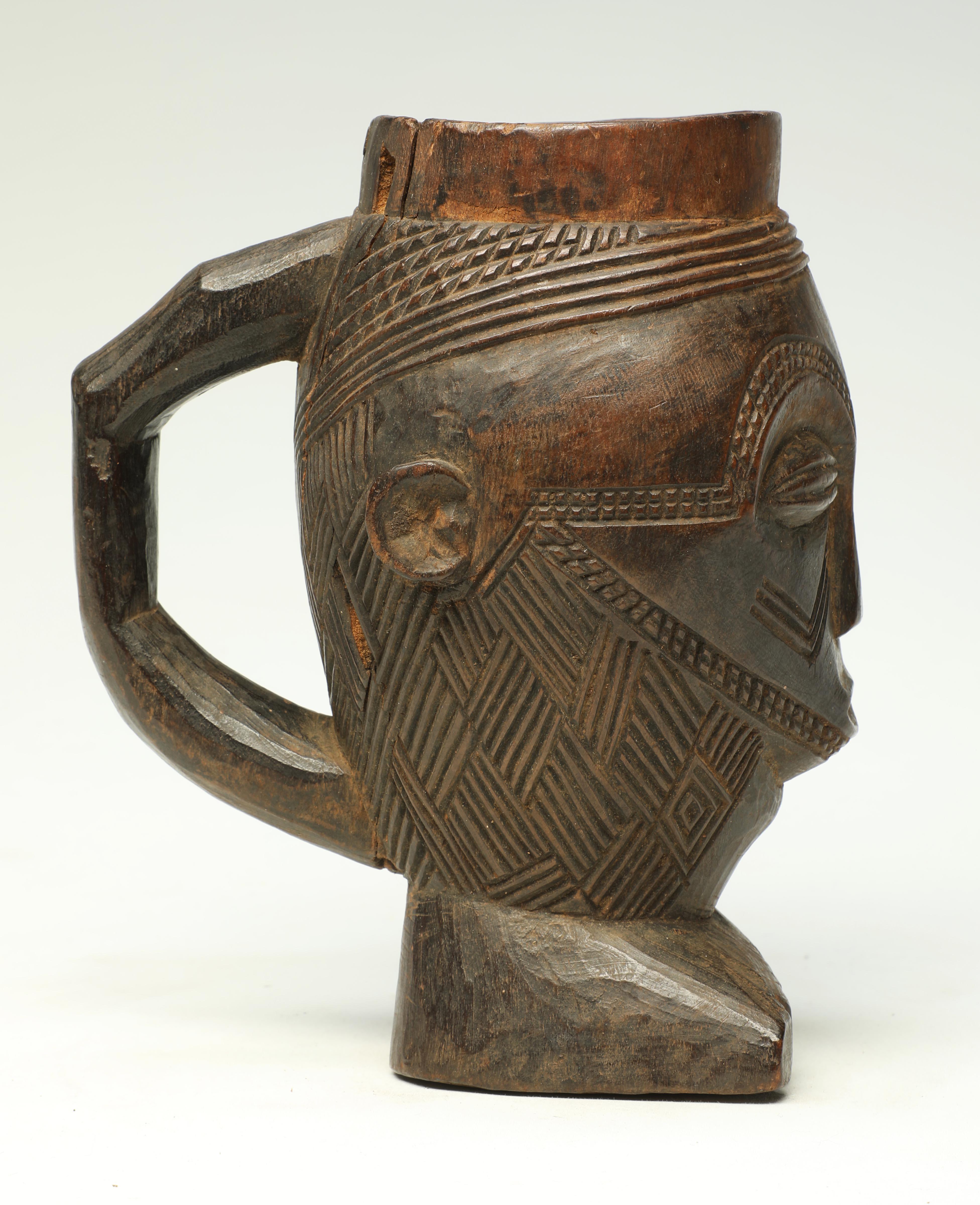 Early finely carved hard wood Kuba figural cup, Congo with rich patina. In the form of a stylized face with the base of the cup a foot. Great incised classic Kuba crisscross design for hair. Deep patina from extensive use, early 20th century. Small