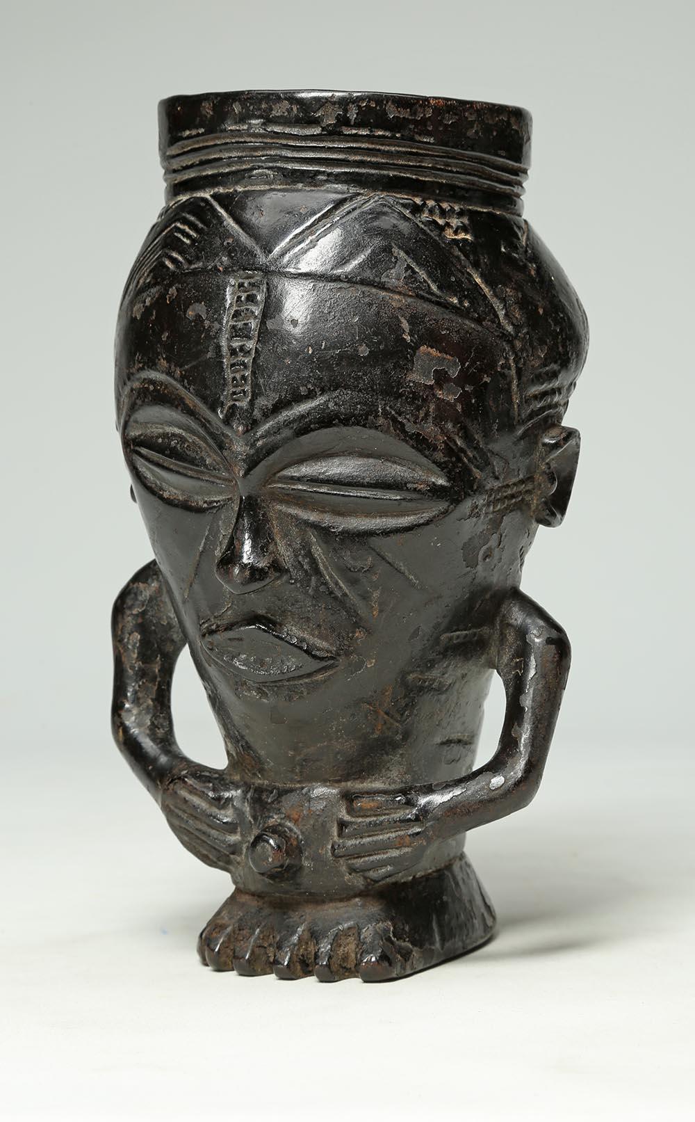 Early finely carved wood tribal Kuba figural cup, Congo with rich dark patina. In the form of a stylized figure with hands on stomach, ending on a foot. Deep patina from extensive use. Early 20th century. Cup 8 x 4 1/2 x 4 1/2 inches. Kuba palm wine