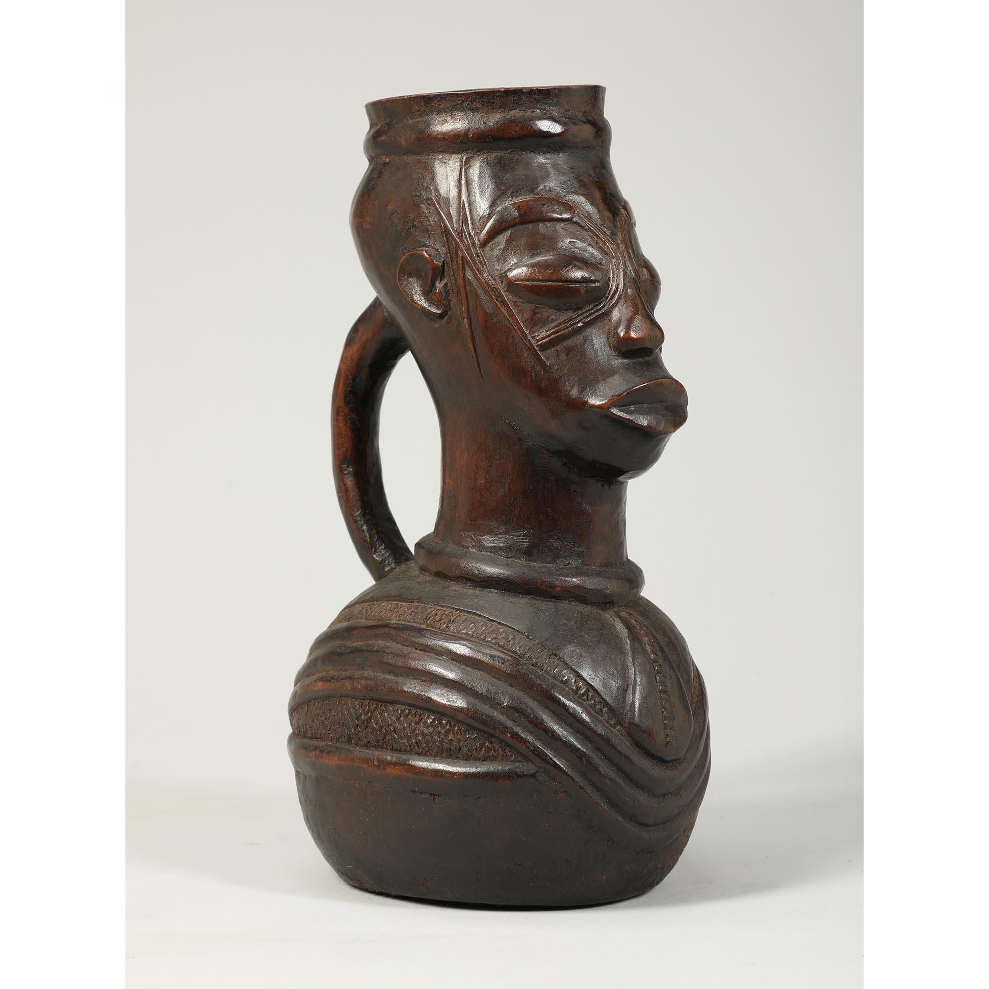Vase rituel Mangbetu en bois sculpté à usage tribal, originaire du Congo, Afrique.
Vase rituel sous forme de pichet en bois avec anse, visage expressif avec scarifications, matière organique sèche à l'intérieur.  Patine profonde due à l'utilisation