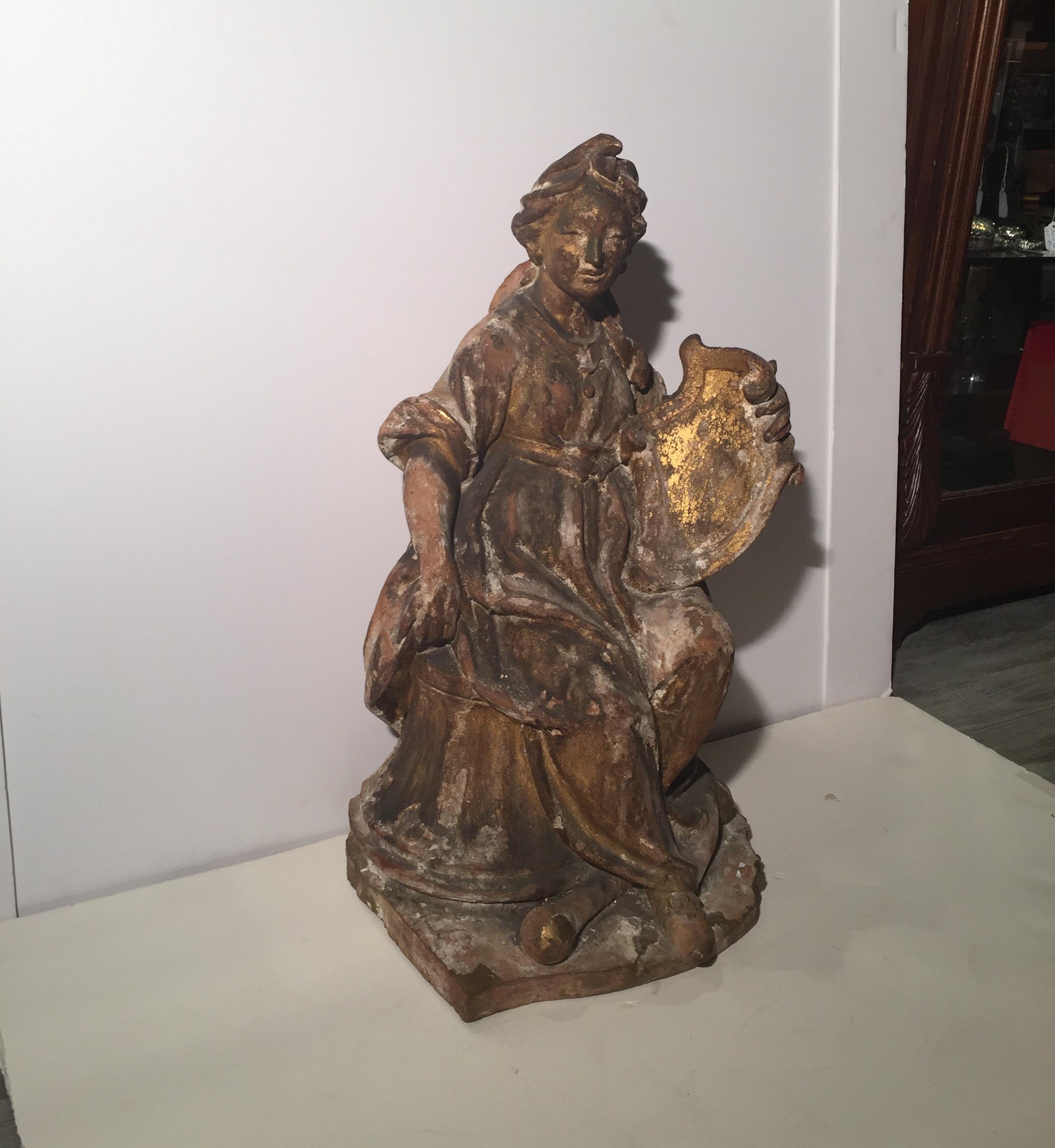 Great early circa 1800 European terracotta figure of a female figure with original worn and weathered finish. The seated figure with shield resting on a base of a neoclassical column. The piece has some chipping and retains some of the original