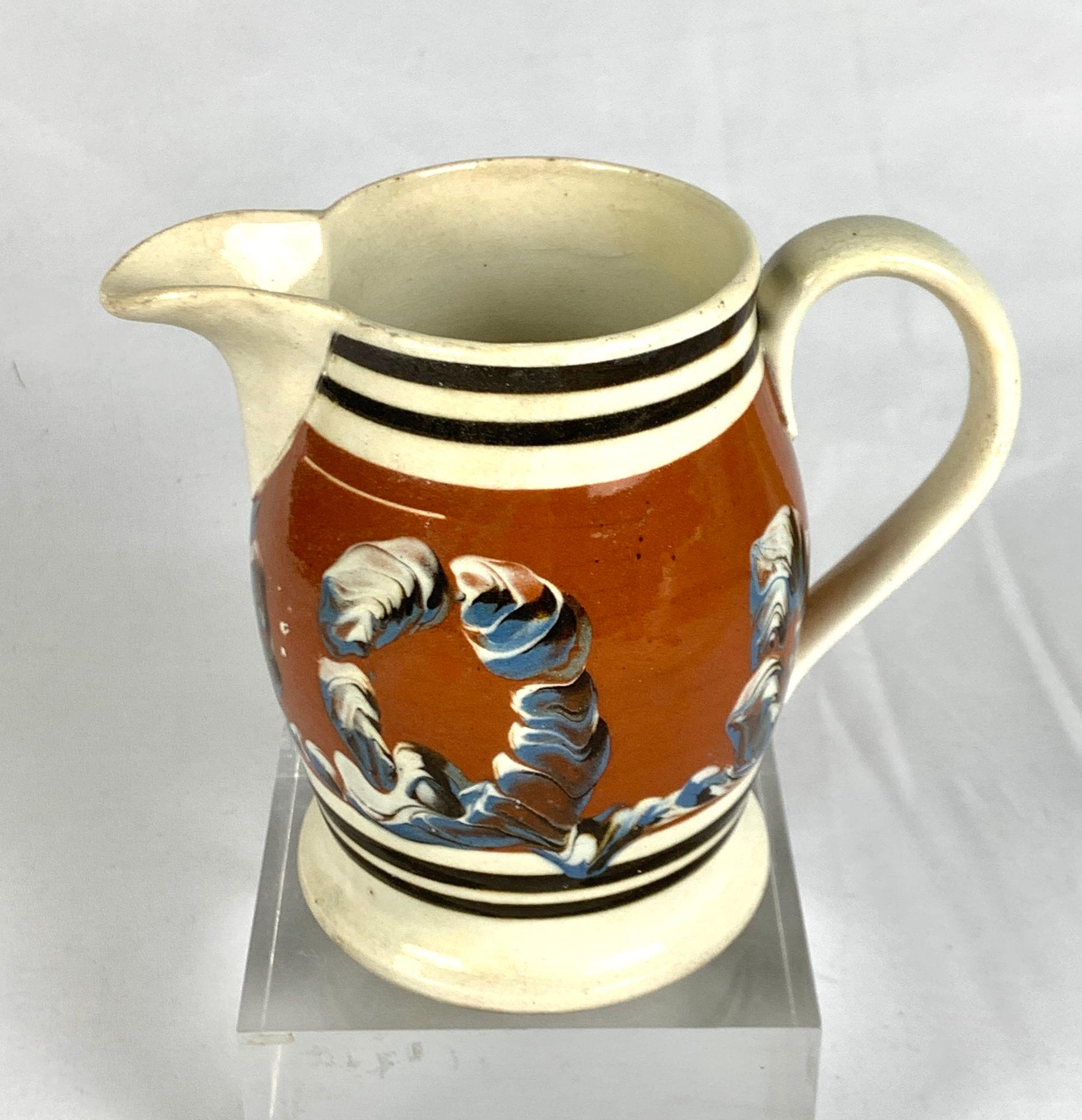 This mochaware pitcher has cable decoration in blue, white, and midnight brown slip on a lovely reddish brown slip ground (see images).
Double bands of midnight brown slip encircle the pitcher above and below the main decoration.
Crafted in England