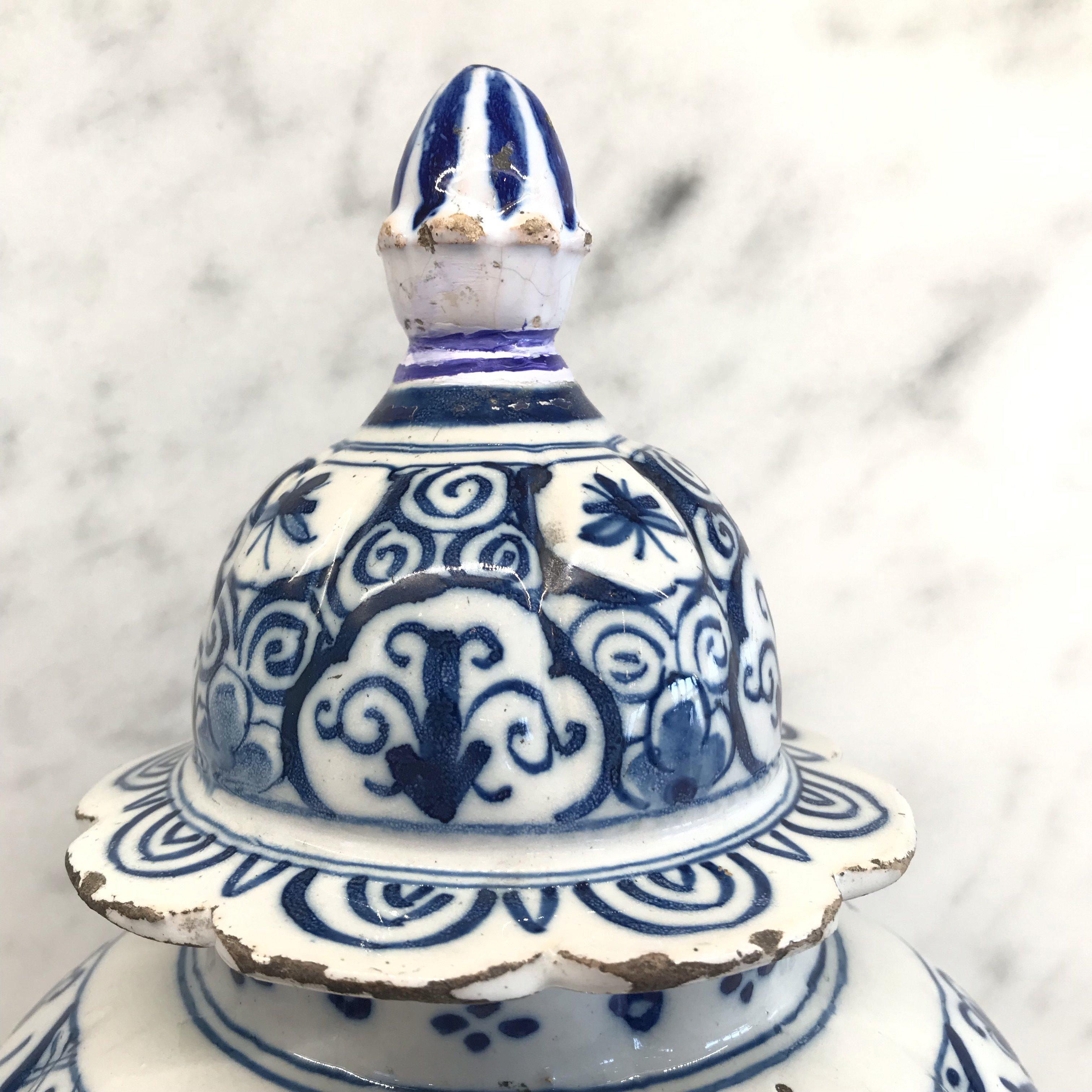 A Delft blue and white covered vase decorated with blue flowers. The cover is topped by a traditional ball finial. The back of the vase is decorated with a single Artemisia leaf. Small edge chips restored, ball finial earlier replacement.
#4278.