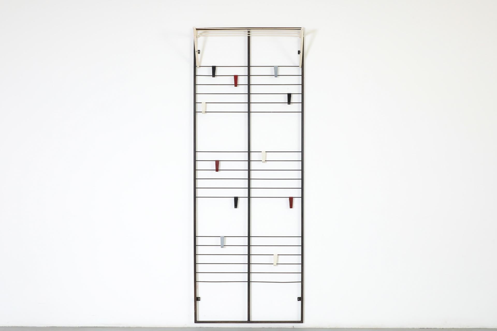 Appendiabiti da parete industriale Coen de Vries in edizione precoce per Devos. Struttura in metallo smaltato nero con un assortimento di ganci in metallo color Bauhaus e un ripiano mobile a doghe bianche. I ganci e la rastrelliera presentano segni