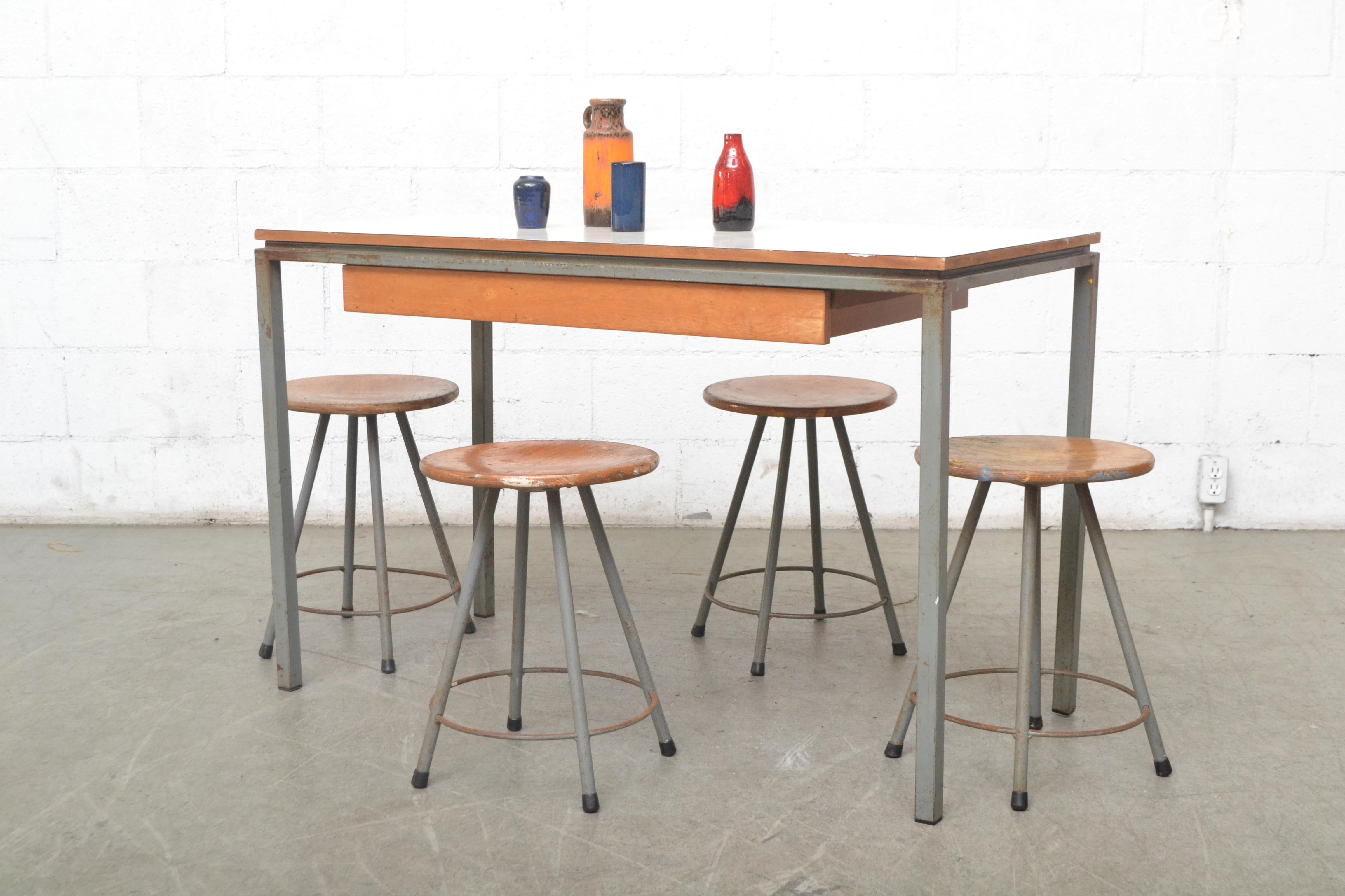 Early edition Marko industrial task or dining table with four matching stools. Both have grey enameled metal tubular frames, lightly refinished natural wood. Table has a white formica top and long storage drawer. Stools measure - 13.25 x 13.25 x