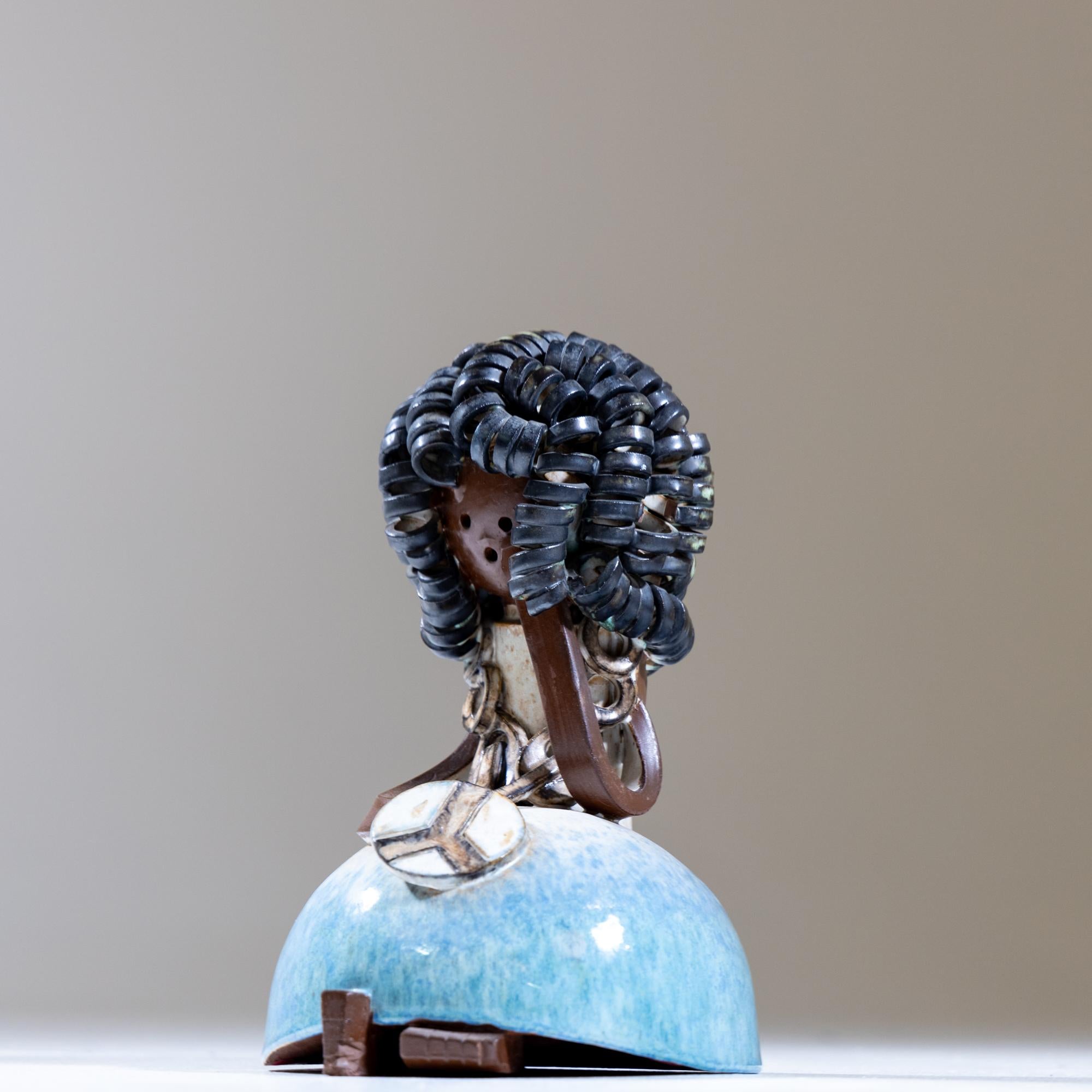 Kleine polychrom glasierte Keramikfigur einer kleinen sitzenden Figur mit lockigem schwarzen Haar und Kette mit Friedenszeichen.