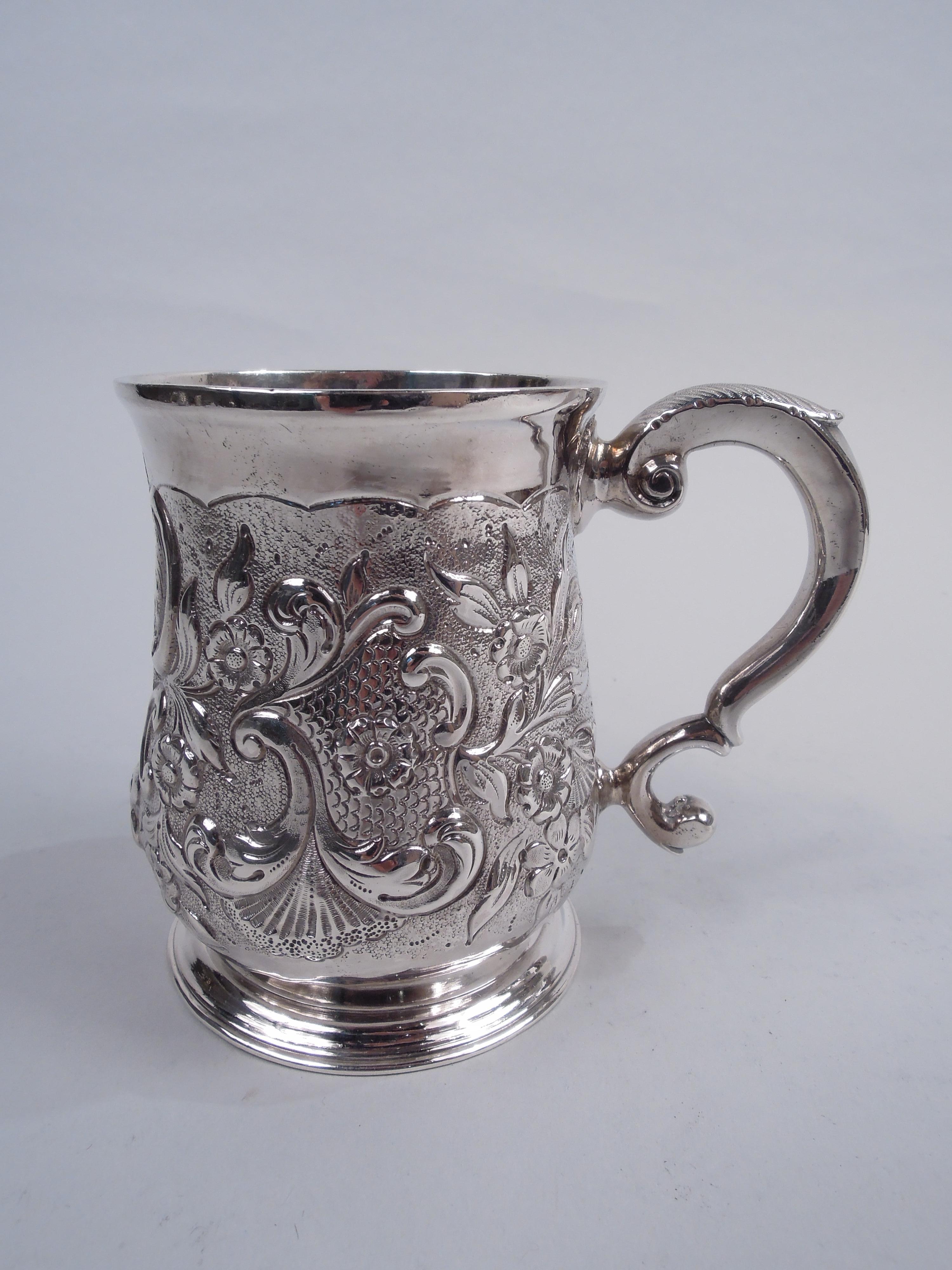 George II sterling silver mug. Made Thomas Tearle in London in 1735. Baluster bowl with leaf-capped double-scroll handle and spread raised foot. Later ornament in form of chased and engraved scrolls, flowers, and scallop shells on stippled ground.