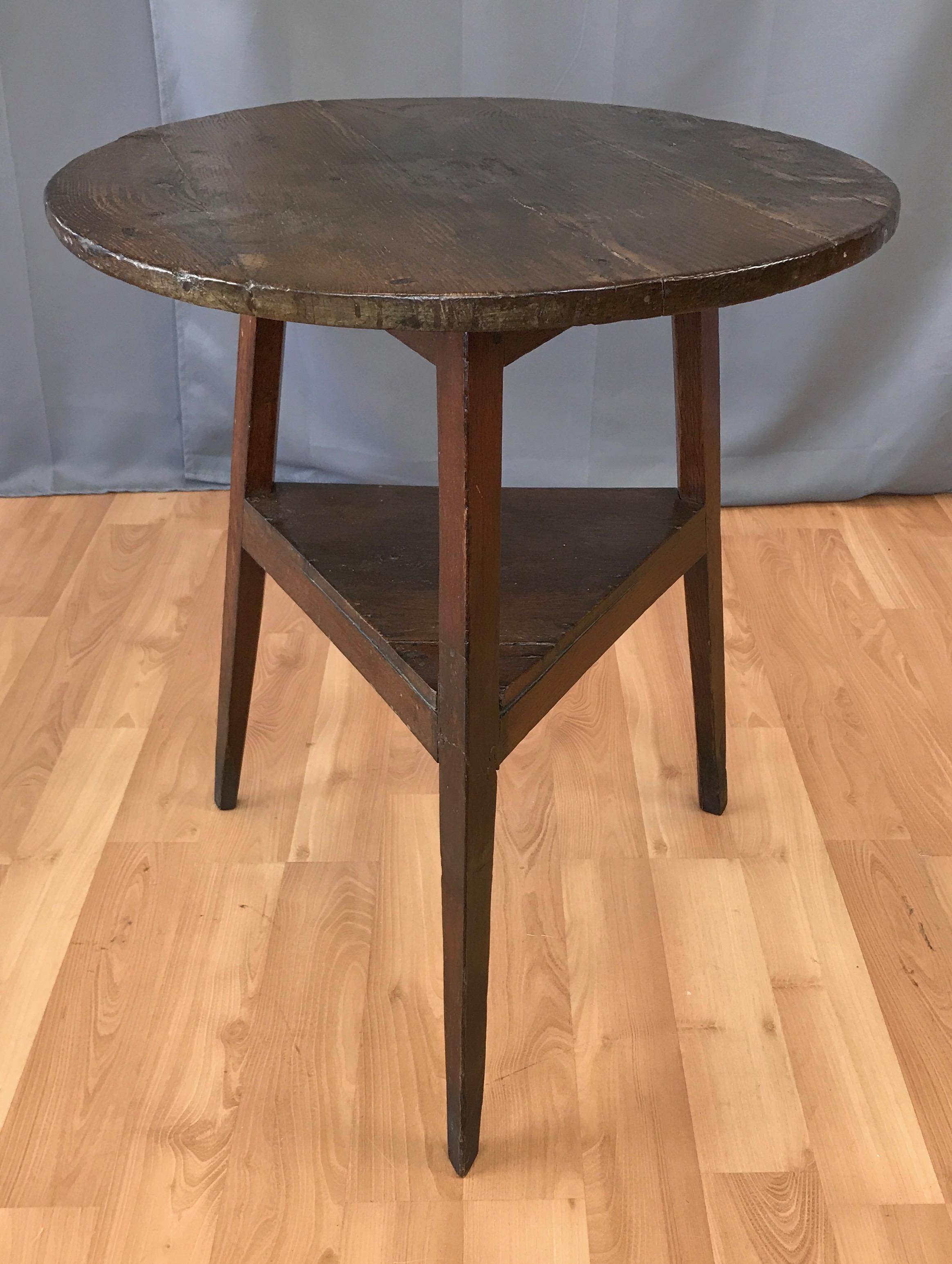 A very handsome Victorian Era English oak cricket table with shelf from the 1850s.

Four-plank circular top over triangular two-plank lower tier, supported by three tapered legs. Craftsman’s hand evident throughout, with planed and shaped elements