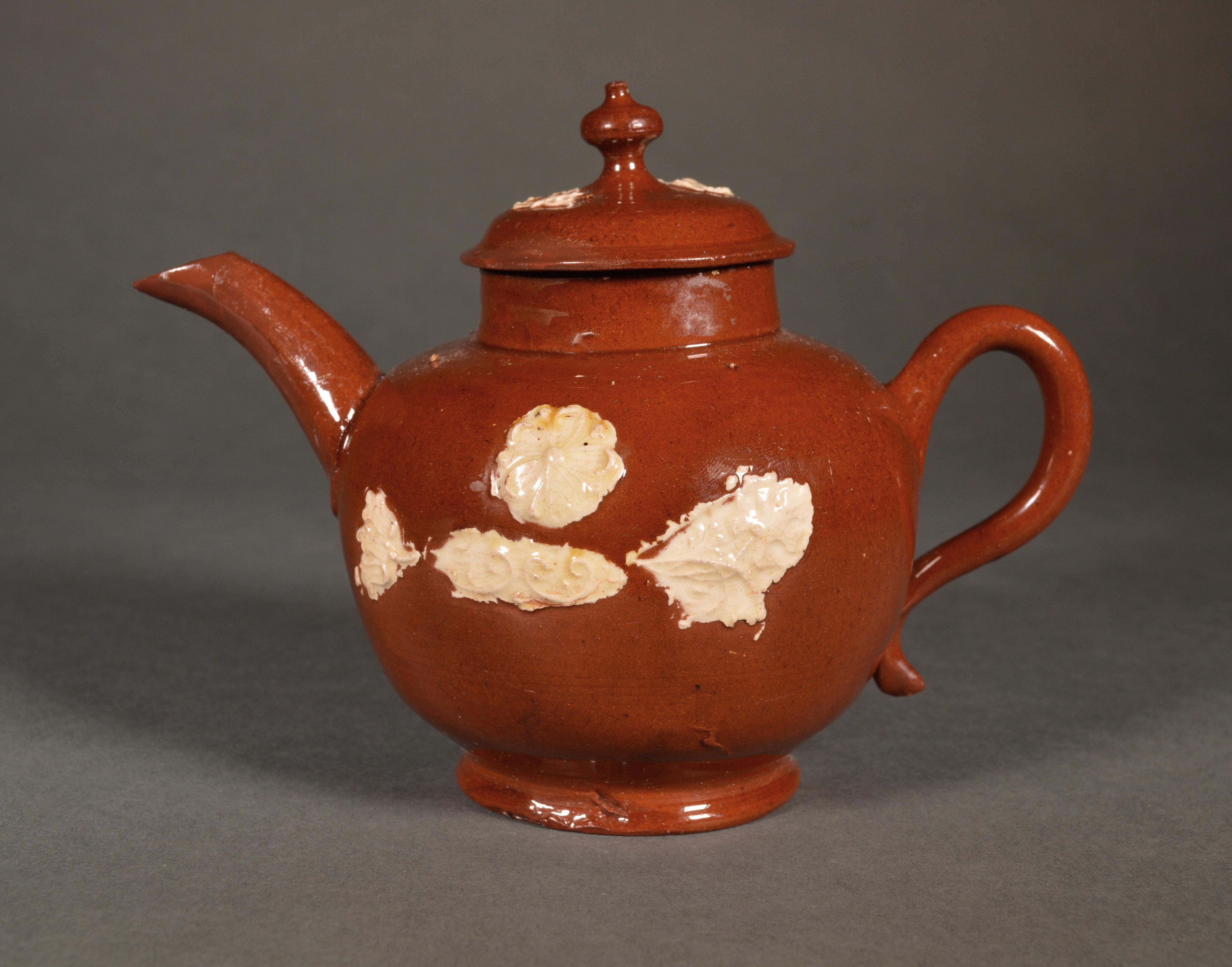 Early English Staffordshire Pottery redware teapot,
1740-1750
(NY8983A/muk)

The small redware pottery lead glaze teapot has a red colored body and sprigged with cream slip on both sides of flowers & leaves.

Reference: The Henry H. Weldon