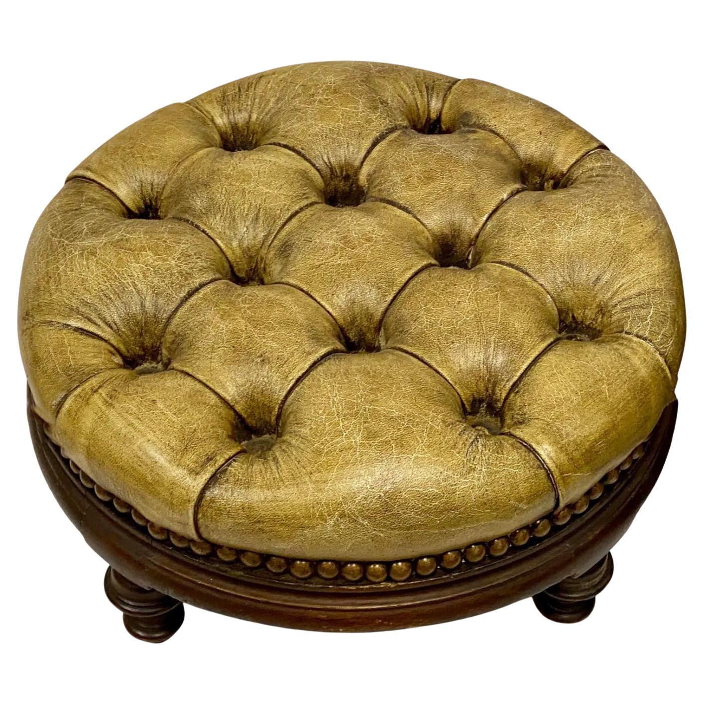 Love these! This is a pair of early English tufted gold leather Chesterfield ottomans on mahogany frames. Note the carved and turned feet!They are unmarked and in very good condition.