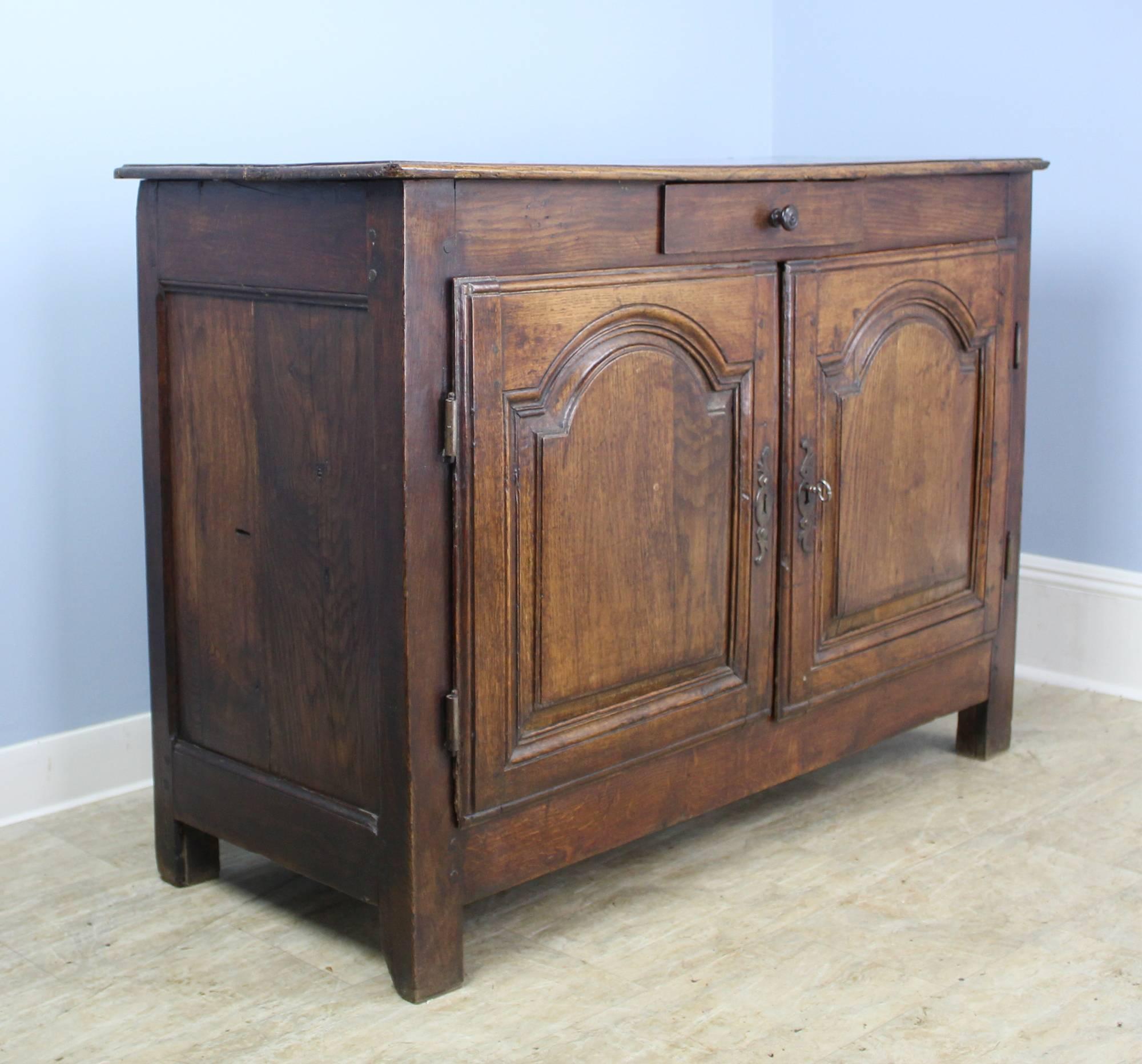 An antique buffet from France. Note the period details: beautifully carved panels on the cabinet doors, original escutcheons and hinges. The oak of this country cupboard is a beautiful color with a rich patina. Single drawer above a cabinet with a