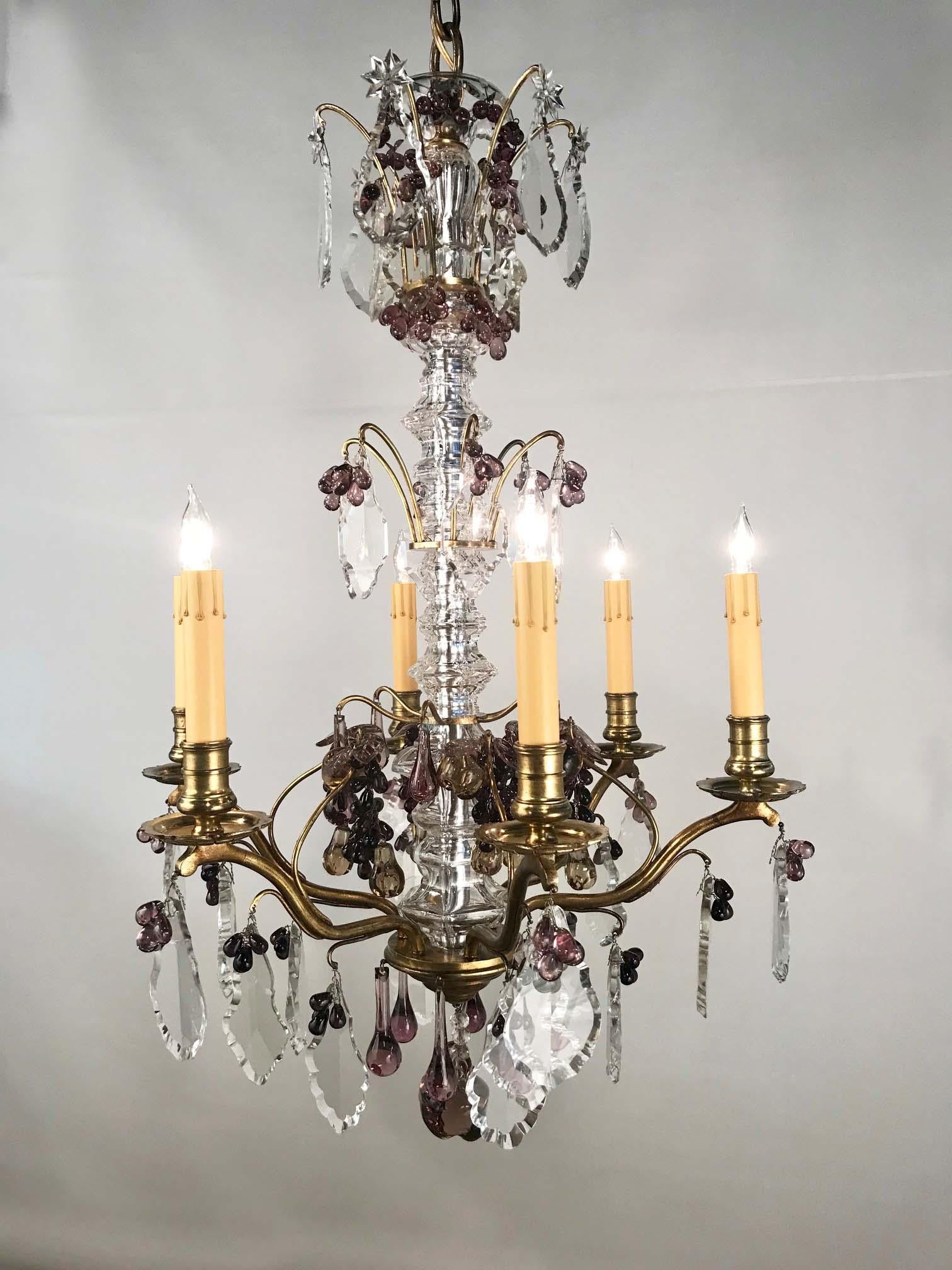 It has a stem sheathed in molded glass. The arms are hung with an unusually good variety of crystals, some amethyst. There are grapes, pendant fruits, leaves and long globular drops, the overall effect is playful yet high quality.