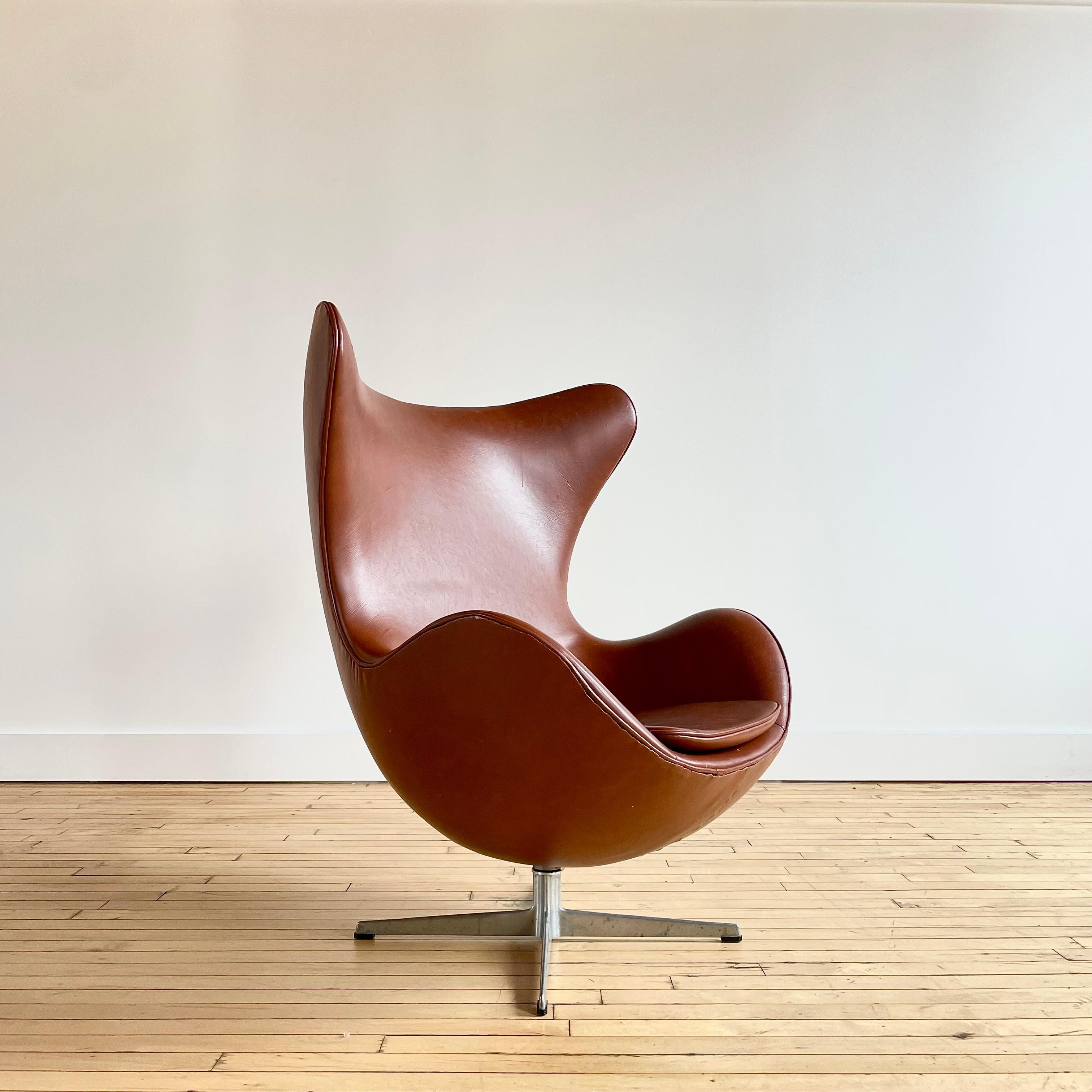 Authentique exemple précoce de l'emblématique Egg Chair d'Arne Jacobsen. La signature de Fritz Hansen est gravée dans la base. 

Cette chaise est recouverte d'un revêtement cognac qui semble être du faux cuir ou du vinyle. Je ne suis pas sûr qu'il