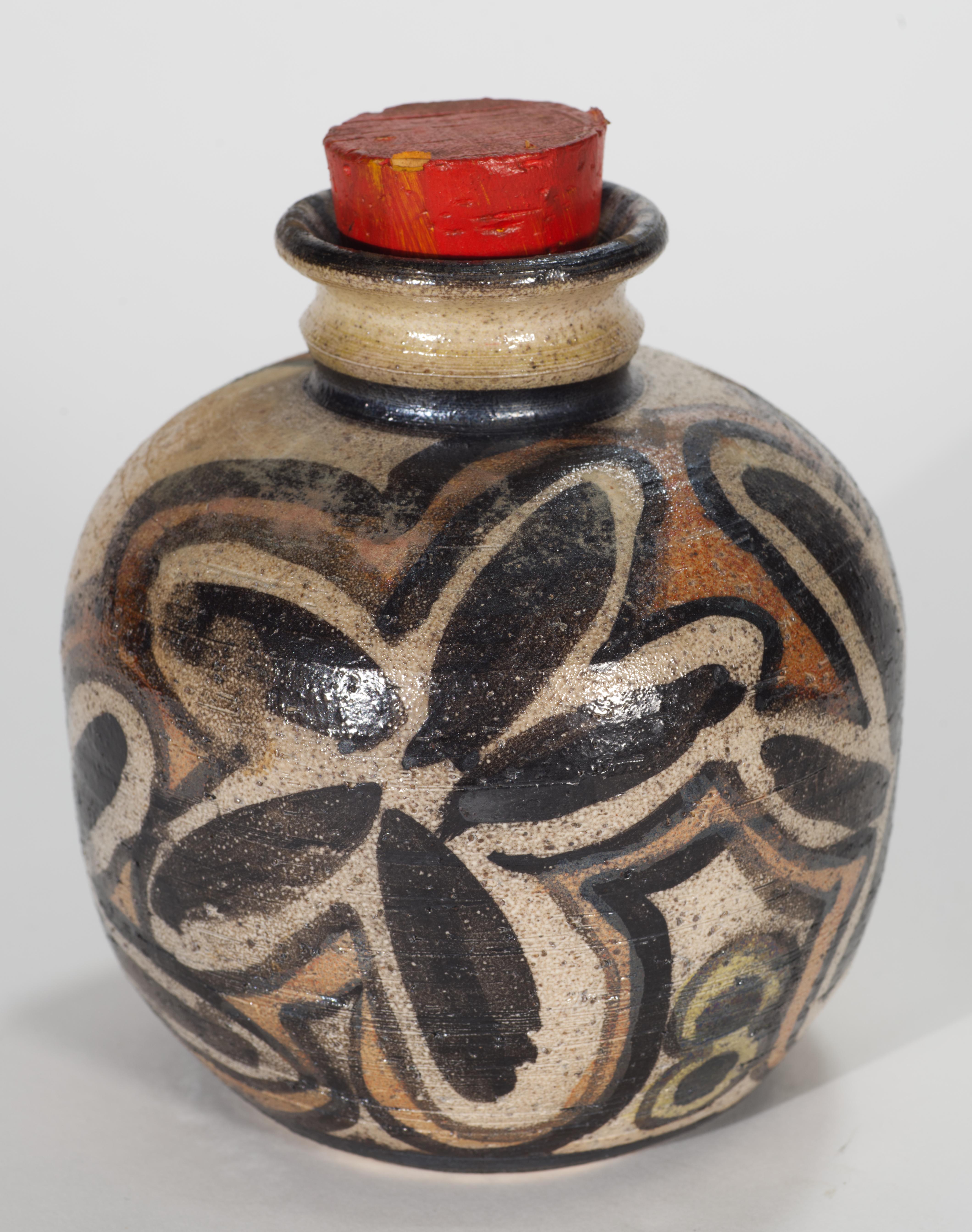 Vaso o barattolo in studio Pottery d'epoca con tappo in legno con decorazioni astratte dipinte a mano in nero, marrone e arancione tenue su sfondo bianco sporco. Lo smalto leggermente strutturato enfatizza l'estetica organica e terrosa del pezzo.
