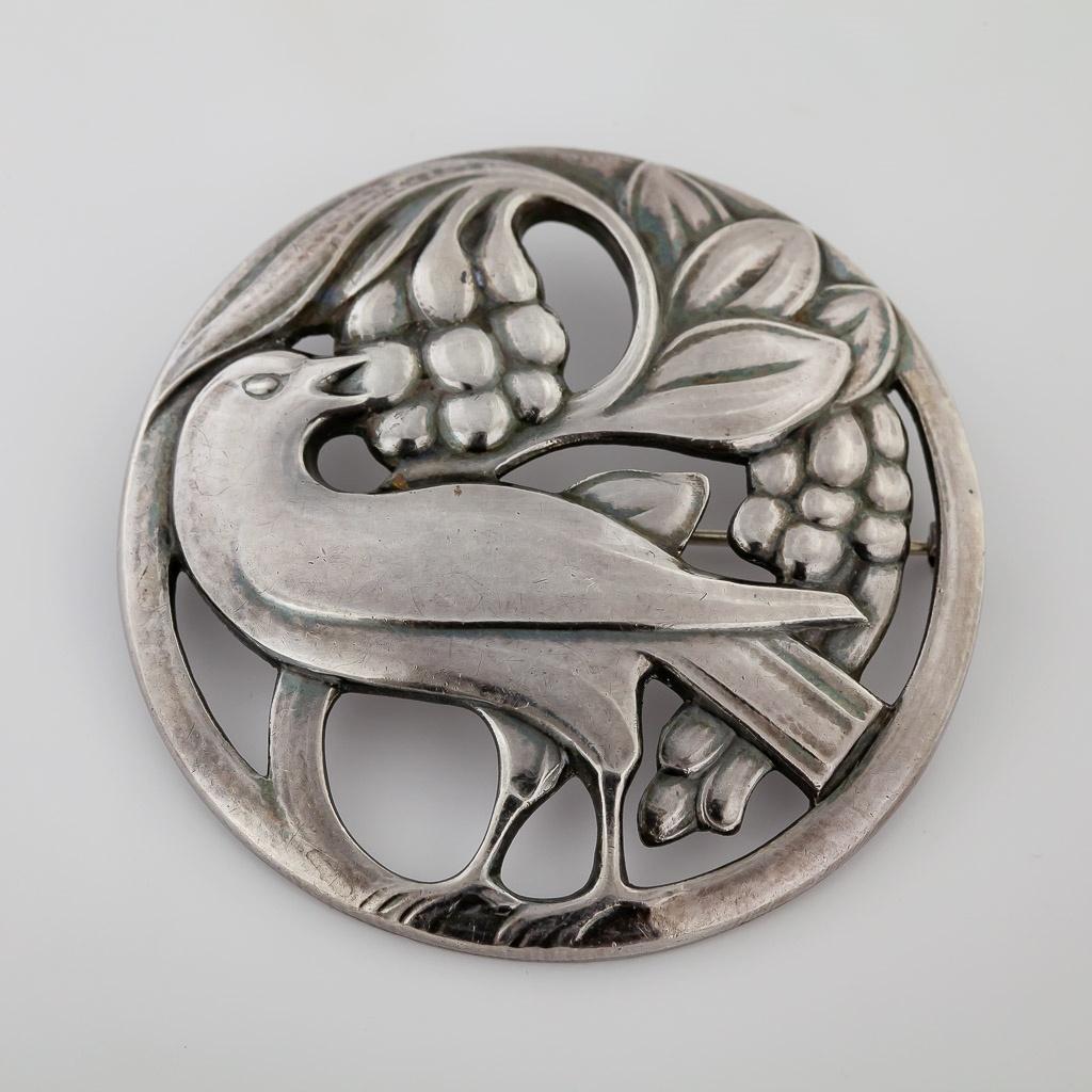 This very early large classic brooch has its original patina, is designed as a bird with berry with open background in sterling silver, 58 mm, marked: 925, Sterling, Denmark, 53, GJ marked (1915-1930), Weight: 24.35 grams. 