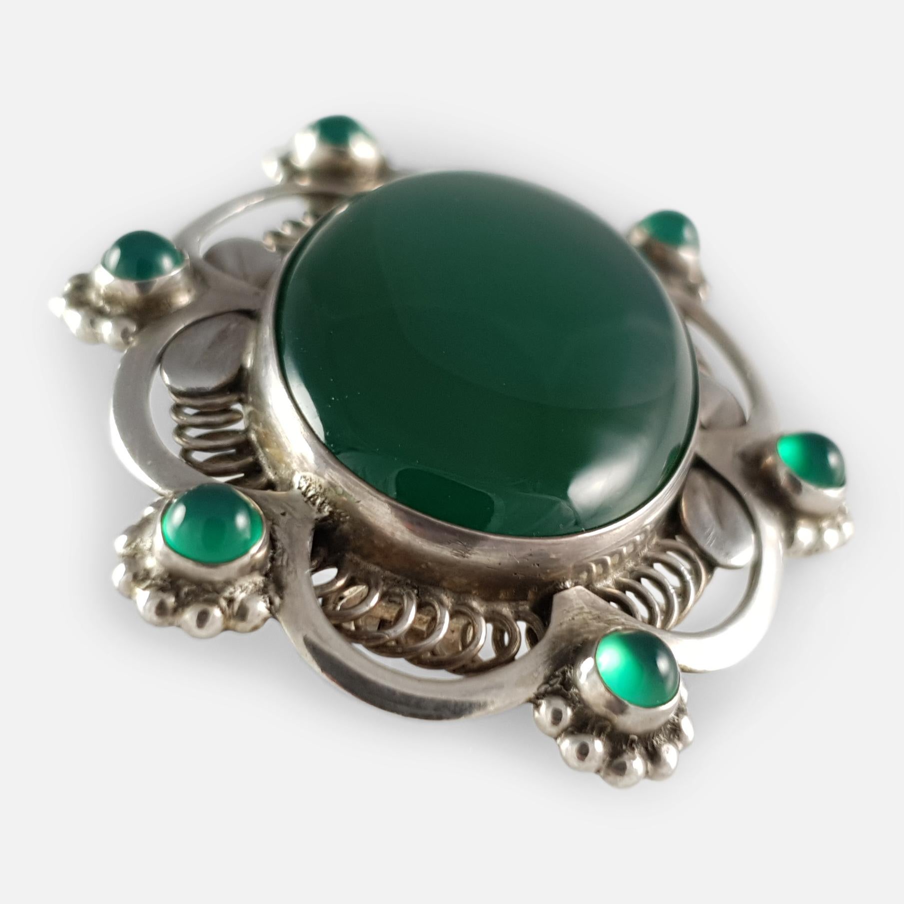 A Georg Jensen silver and green agate brooch #157, circa 1915-1930.  The oval green agate cabochon is set within a beaded wirework and scallop-edged frame, set with six further green agate cabochons. 

The brooch is stamped with the Georg Jensen